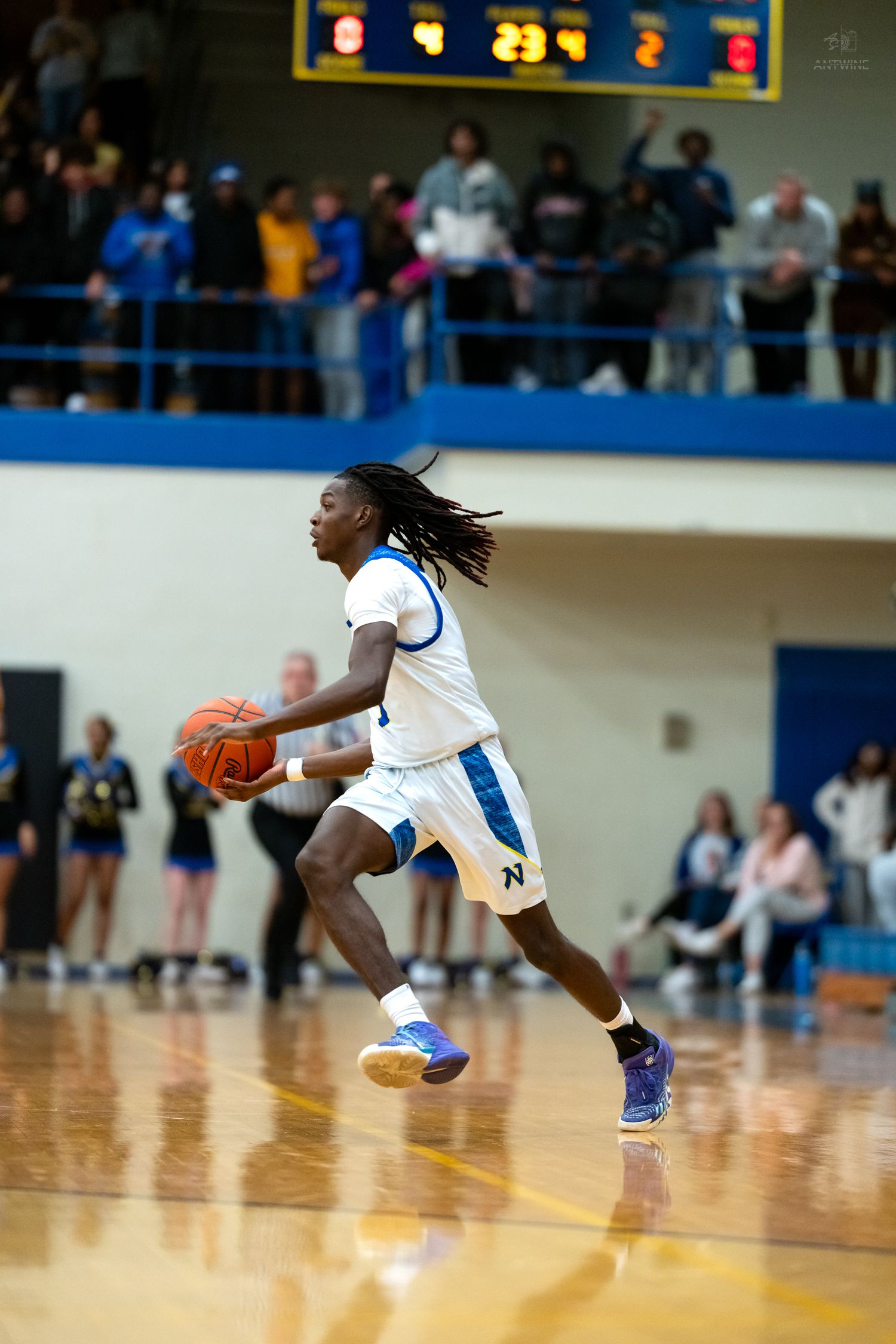 A basketball player with dreadlocks drives the ball down the court in a white uniform.