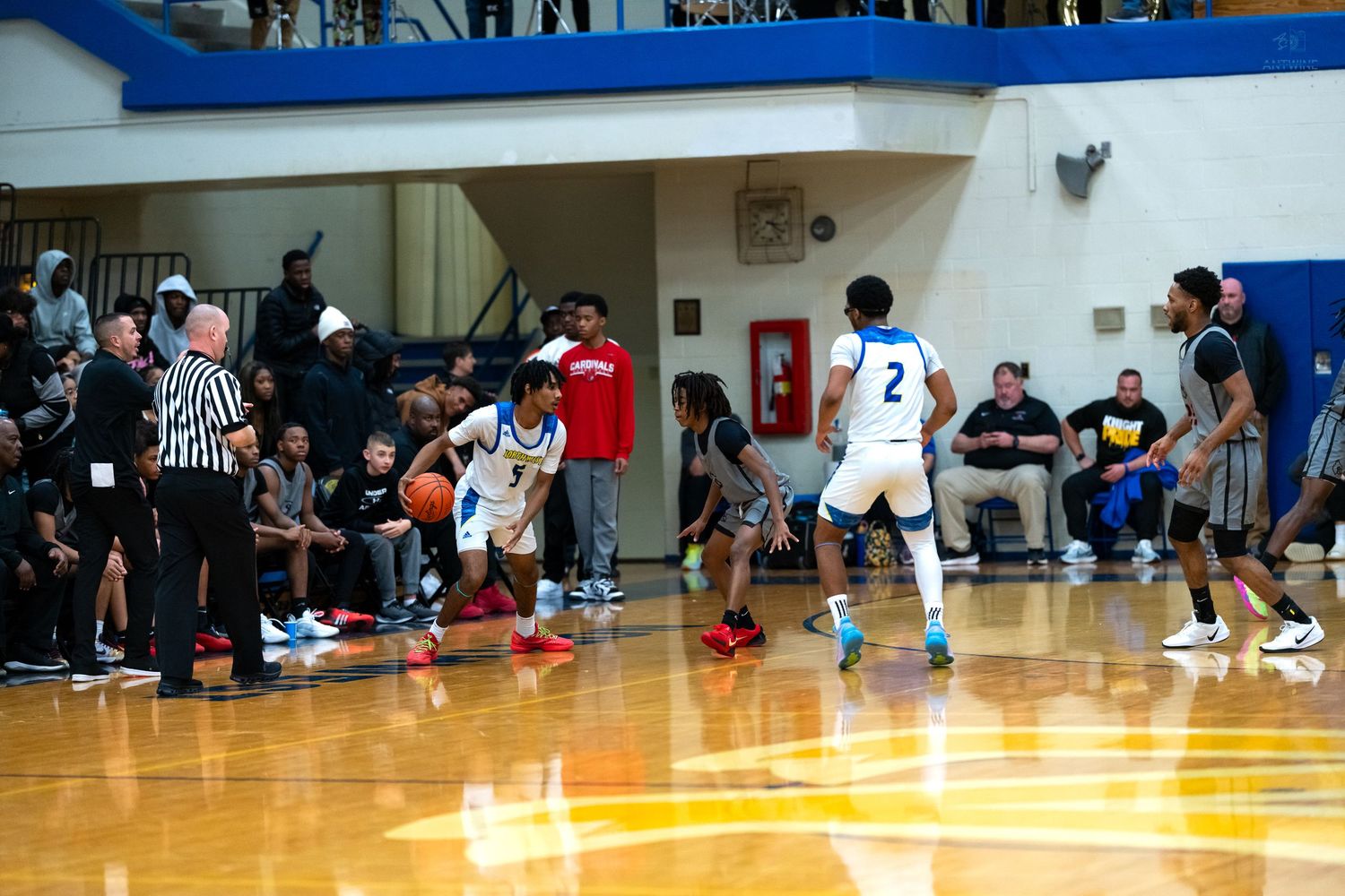 High school basketball players in white and blue uniforms execute a play near the sideline during a game.