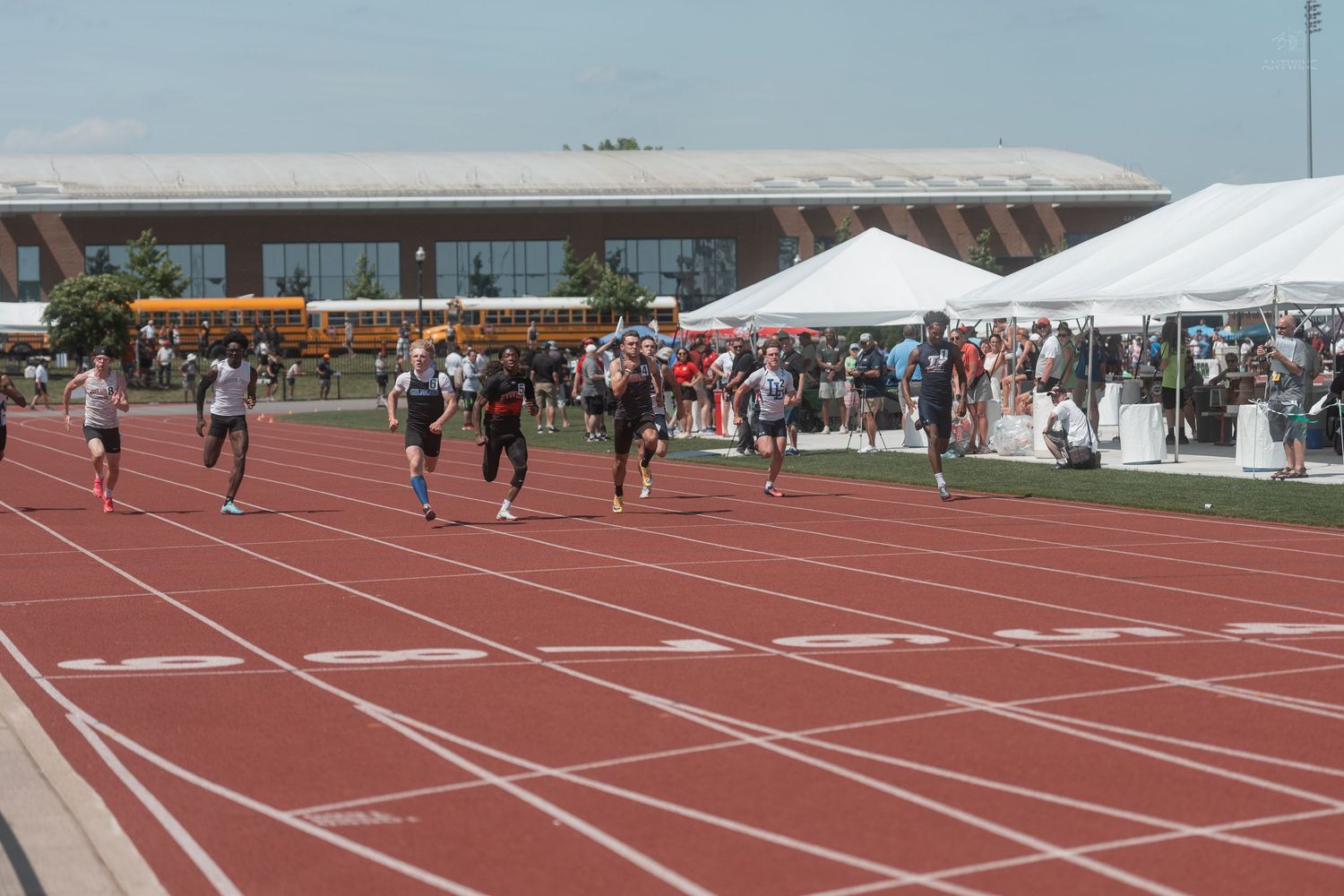 Athletes compete in a track race at an outdoor stadium during a sunny day track and field meet.