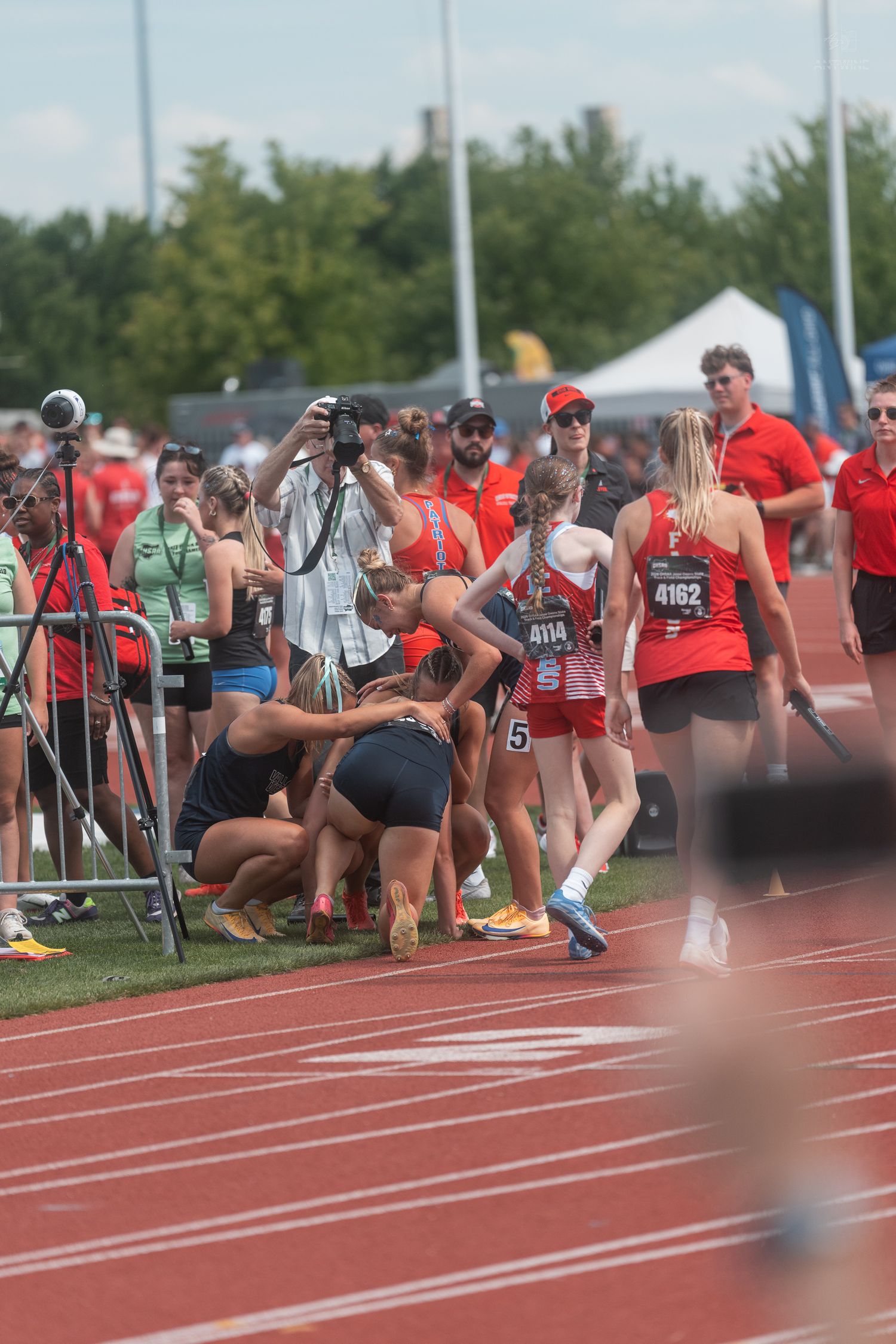 Female track athletes and coaches gather near the finish line after a relay race at an outdoor track meet.