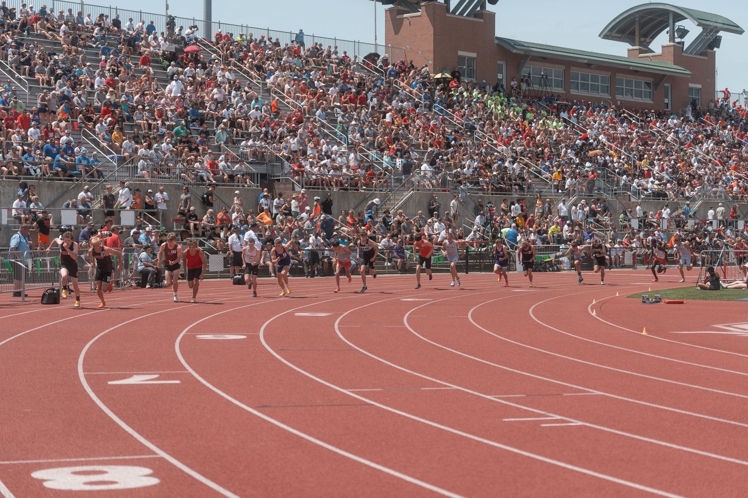 Athletes race around the curve of a red track during a competitive meet at Ohio State University stadium.