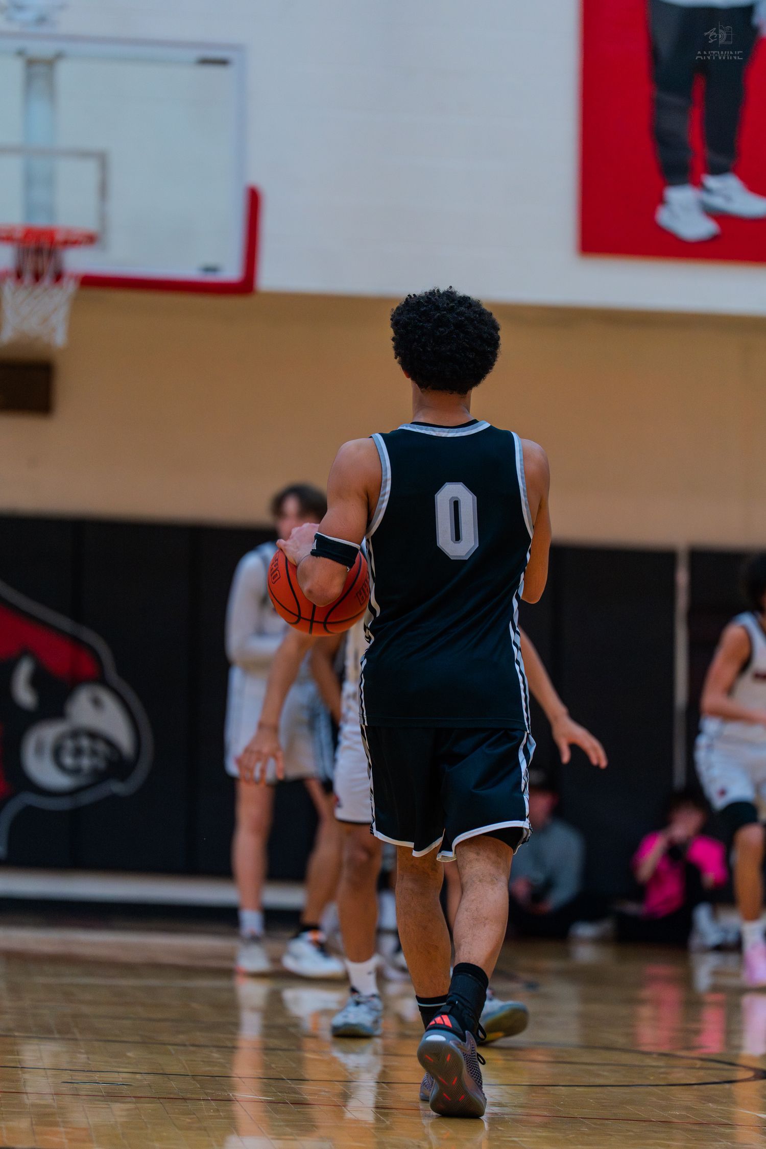 High school basketball player #0 in dark jersey dribbles ball during an indoor basketball game.