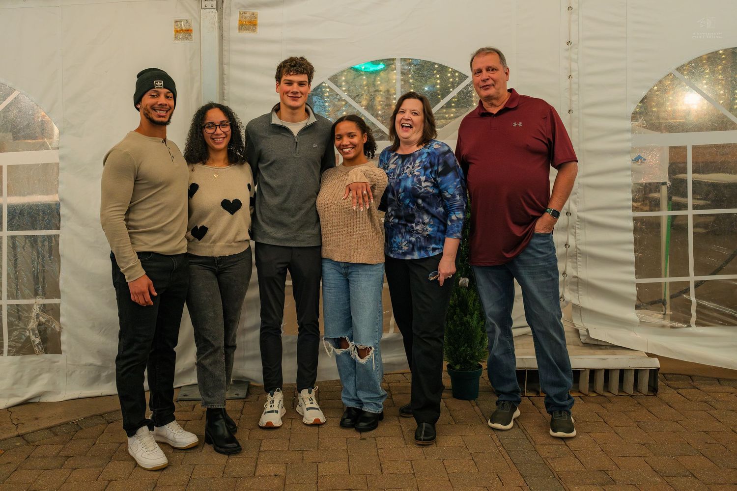 Family group of six people smiling together inside a decorated white event tent at a celebration.
