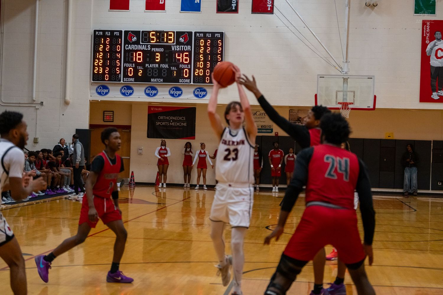 Player number 23 shoots a jump shot over defenders during a close high school basketball game.
