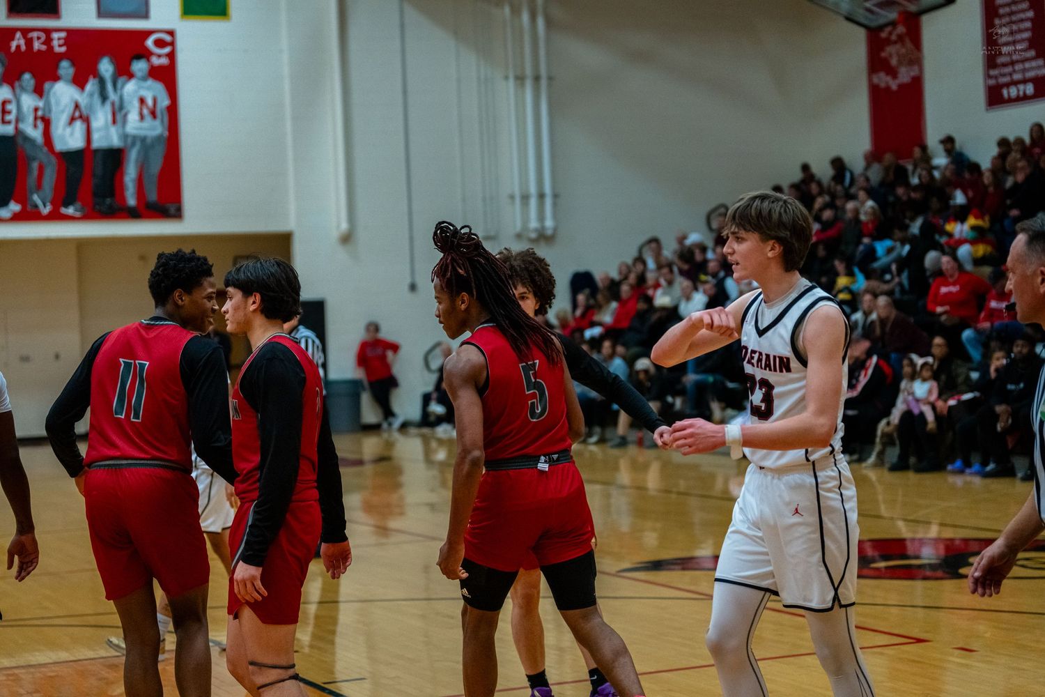 High school basketball players shake hands on court after game with crowd visible in background.