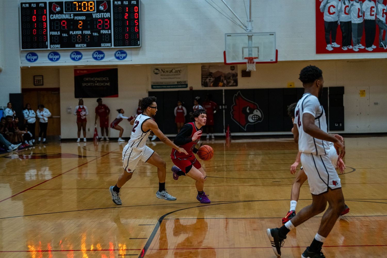Basketball player in red drives toward basket during competitive high school gym game.