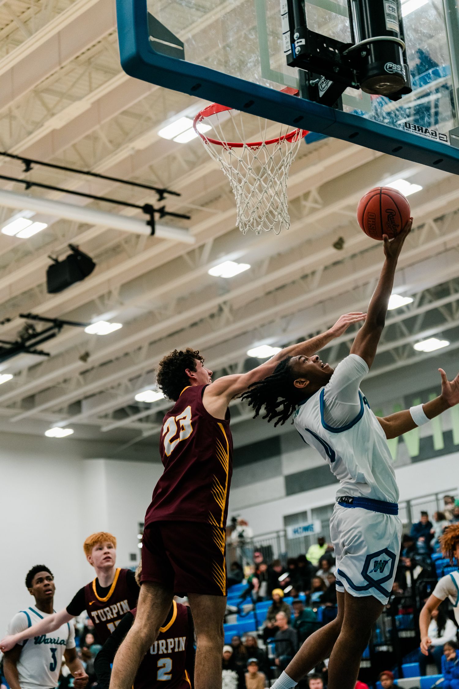 A home team player attempts a layup against a defender wearing #23 Turpin jersey in a packed high school gym.