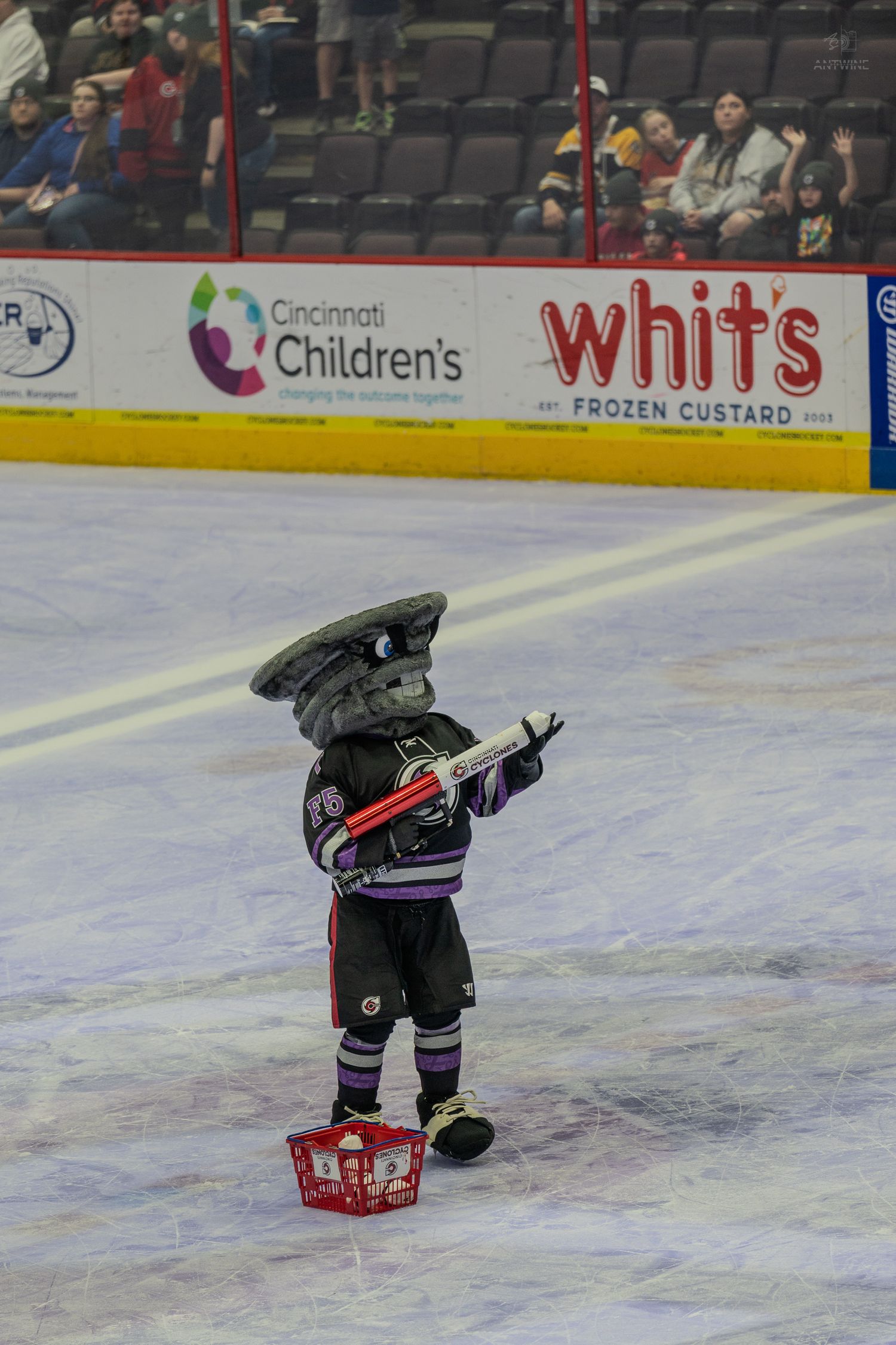 Cincinnati Cyclones hockey mascot skating on ice holding a toy gun during game.