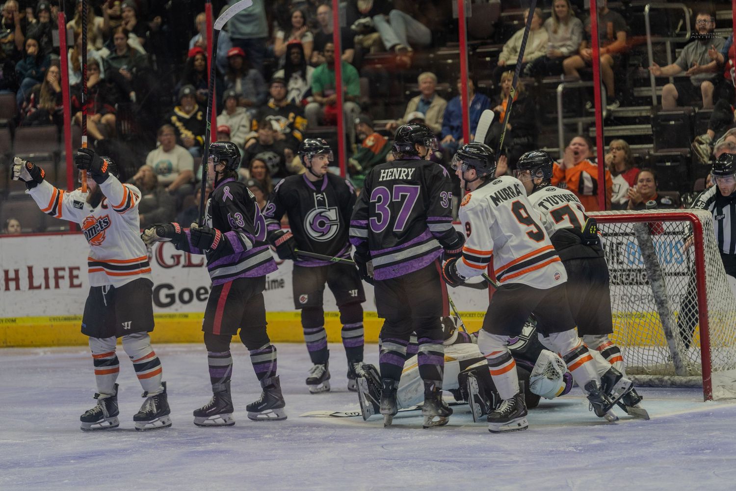 Hockey players from two teams react near the goal crease during an intense minor league hockey game moment.