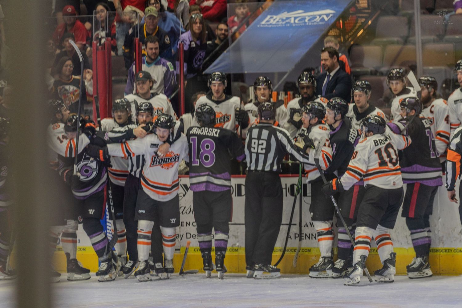 Players and officials gather in a large scrum on the ice during a heated minor league hockey game altercation.