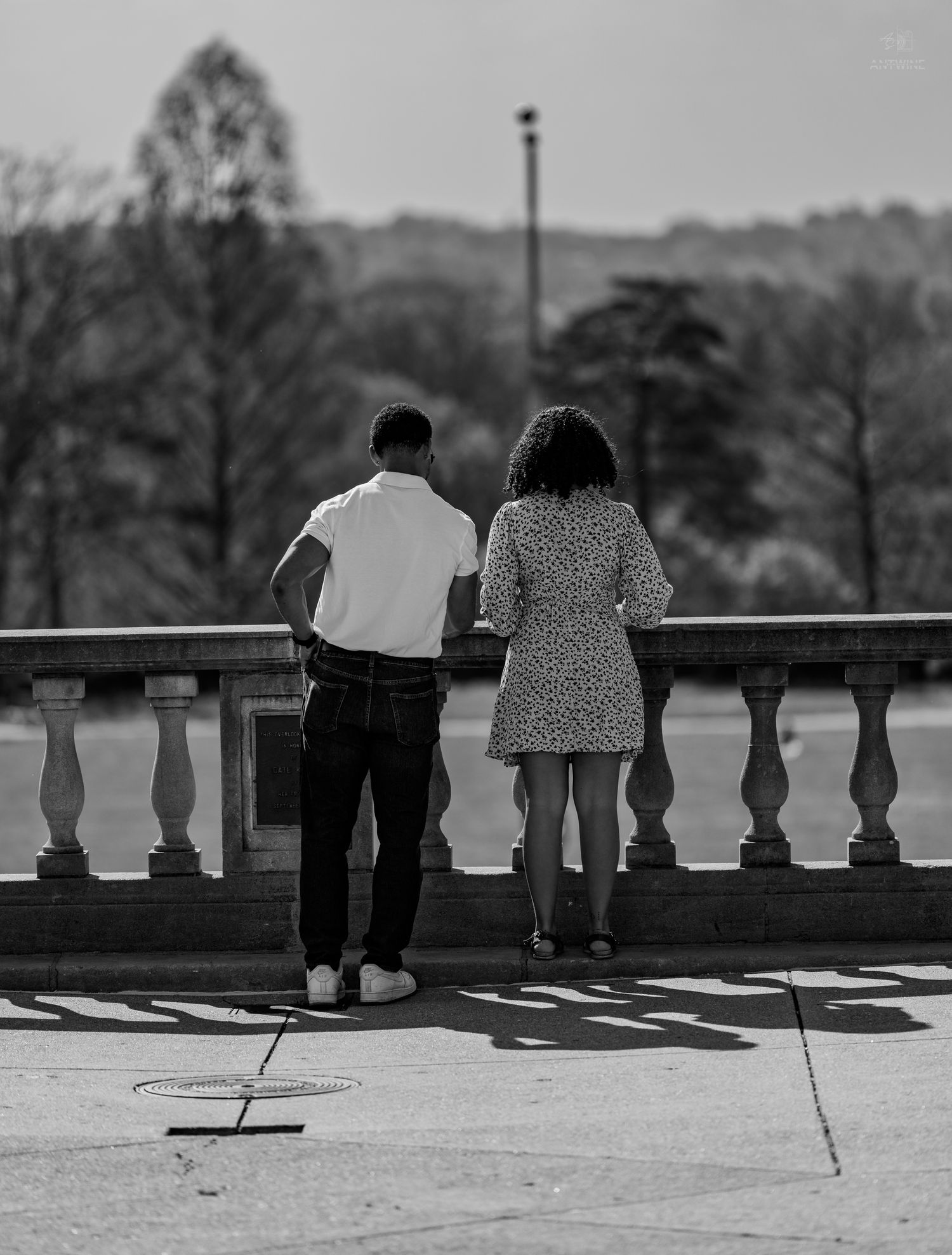 Black and white image of couple leaning on decorative stone balustrade in park setting.