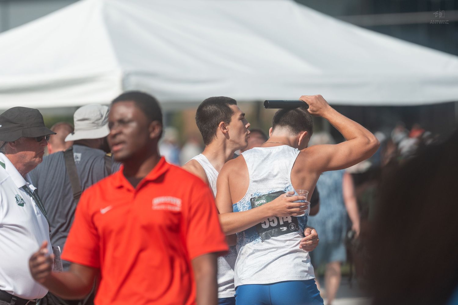 Athletes embrace and celebrate at an outdoor track and field event with officials and spectators nearby.