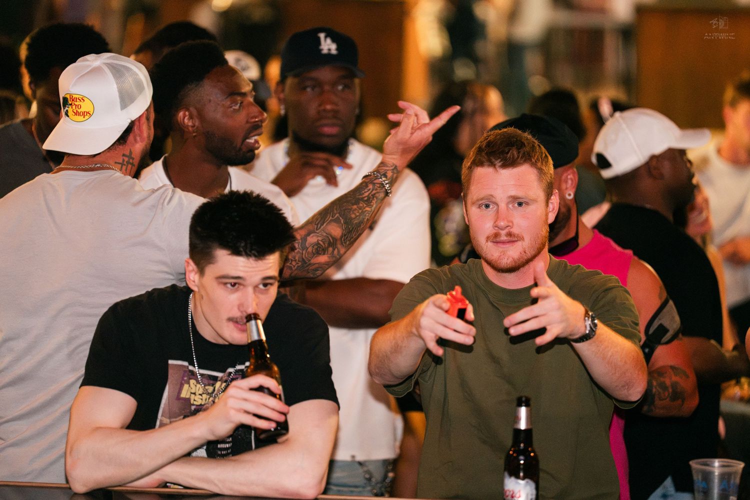 Two men drinking at a bar counter surrounded by a lively crowd at a nightclub.