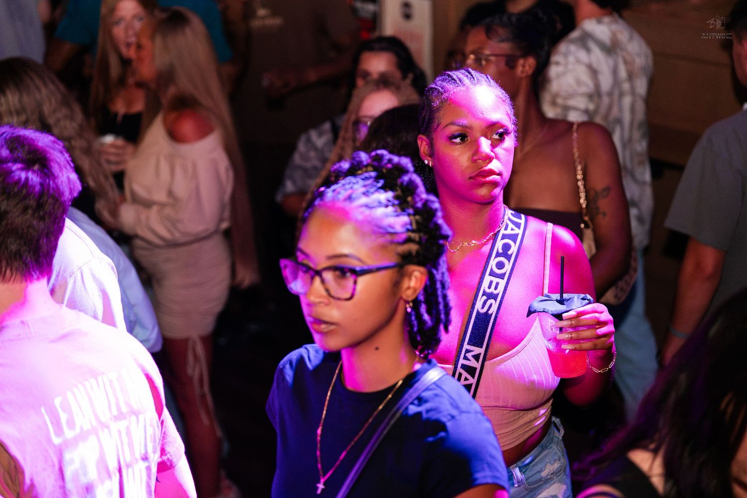 Two young women under purple lights at a crowded indoor social gathering event.