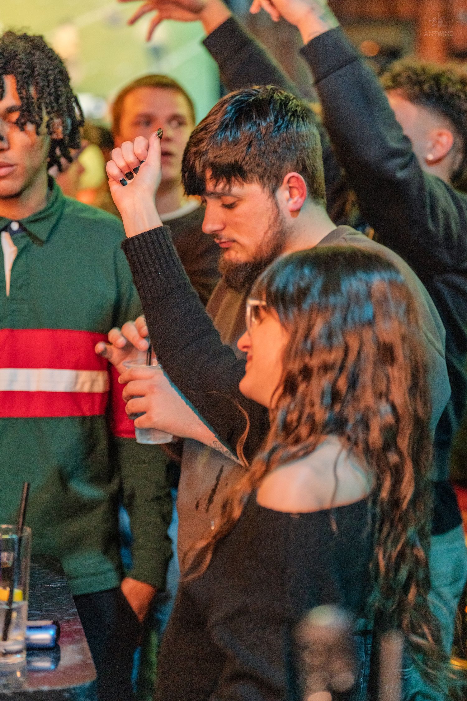 Young couple dancing together at a lively indoor party or bar event with raised hands.