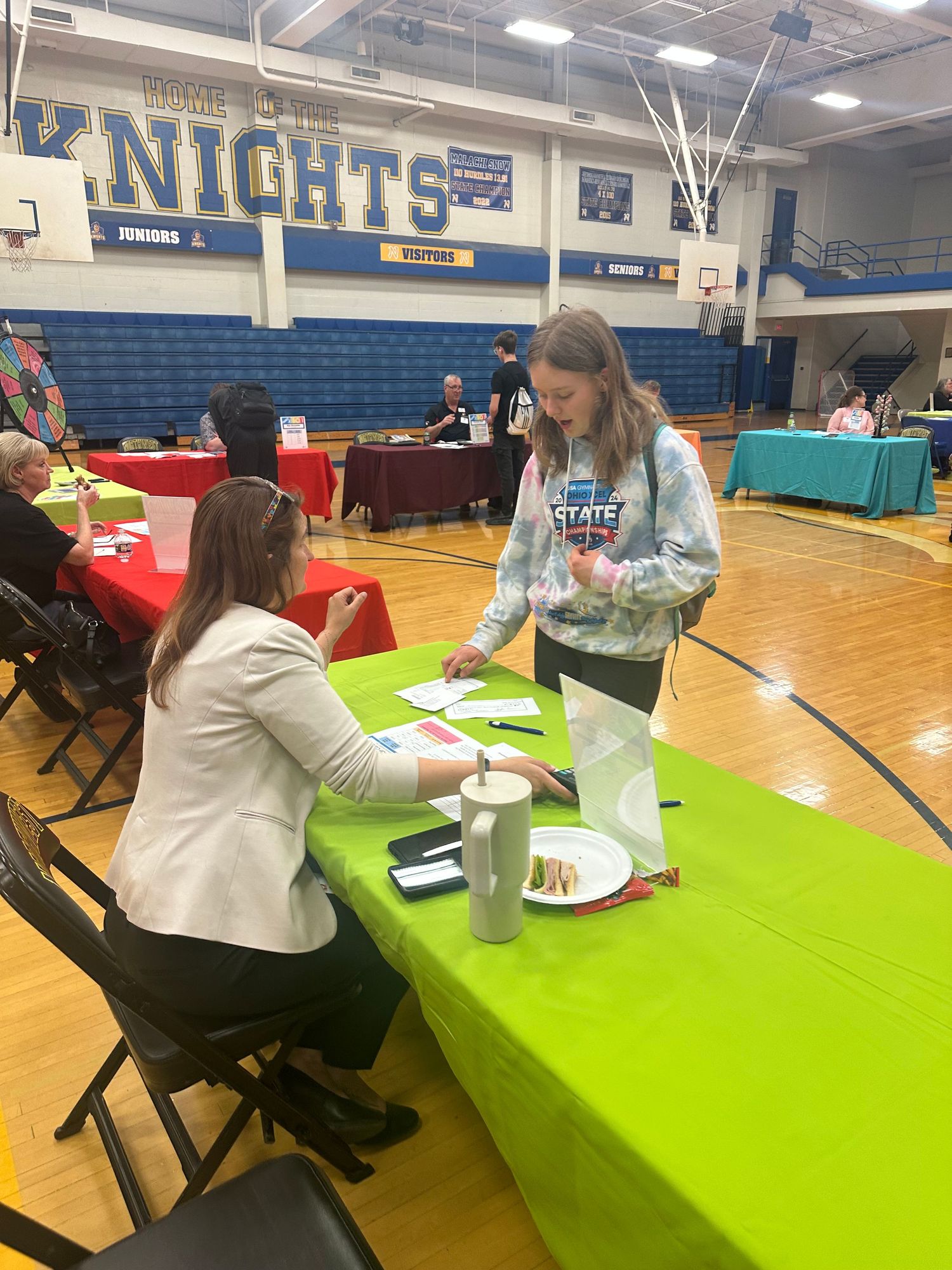 A student reviews documents with a seated recruiter at a green table during a school career fair in a Knights gymnasium.