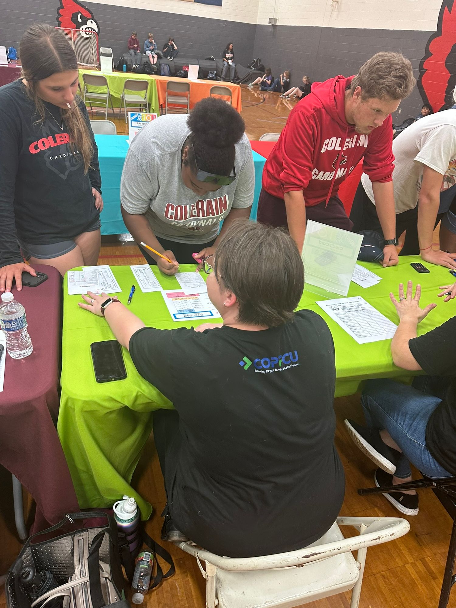 Students signing documents at green tables during a Colerain Township community resource fair event in a gymnasium.