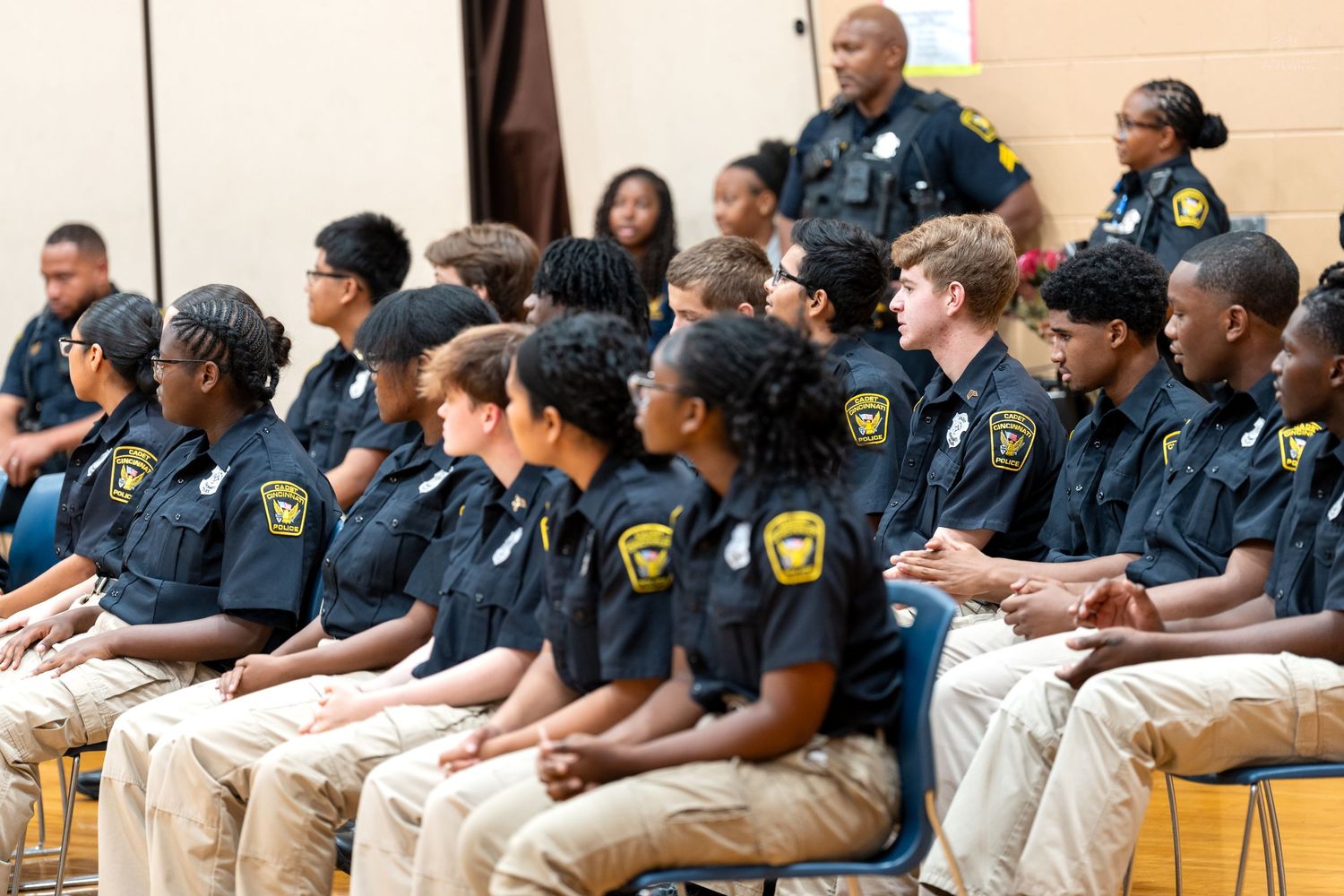 Young police cadets in uniform sit in rows during an official ceremony or training program event.
