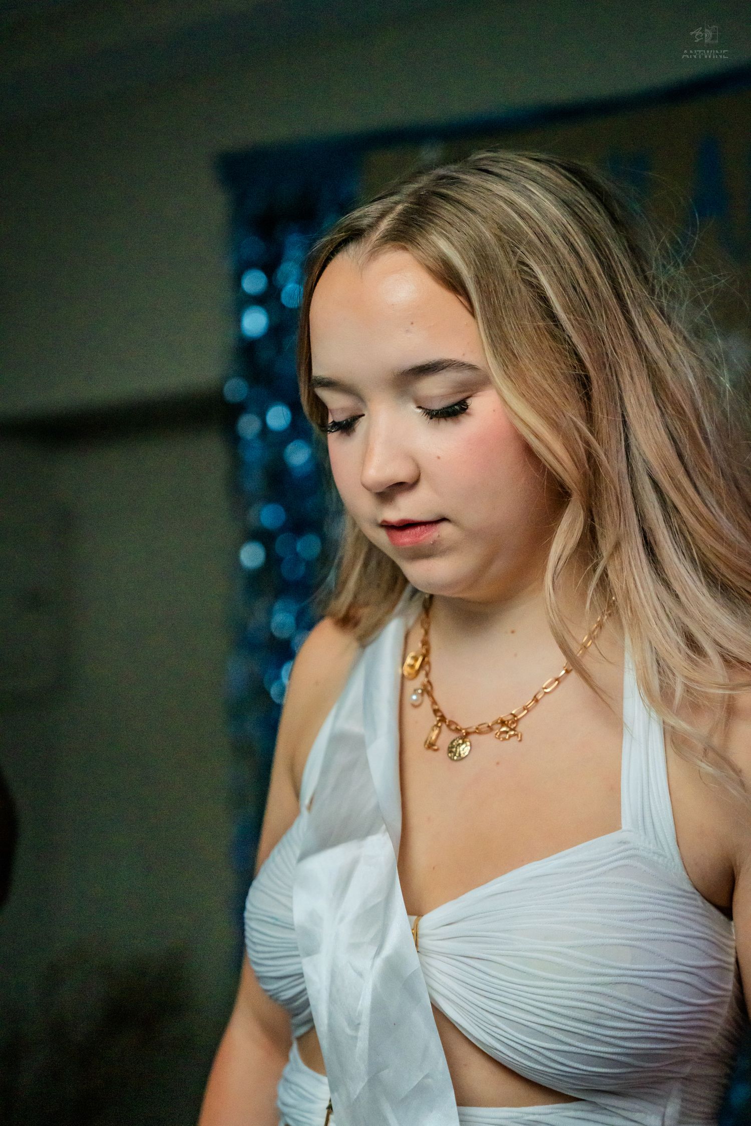 Young blonde woman in white halter top with gold necklace looking down at a birthday celebration.
