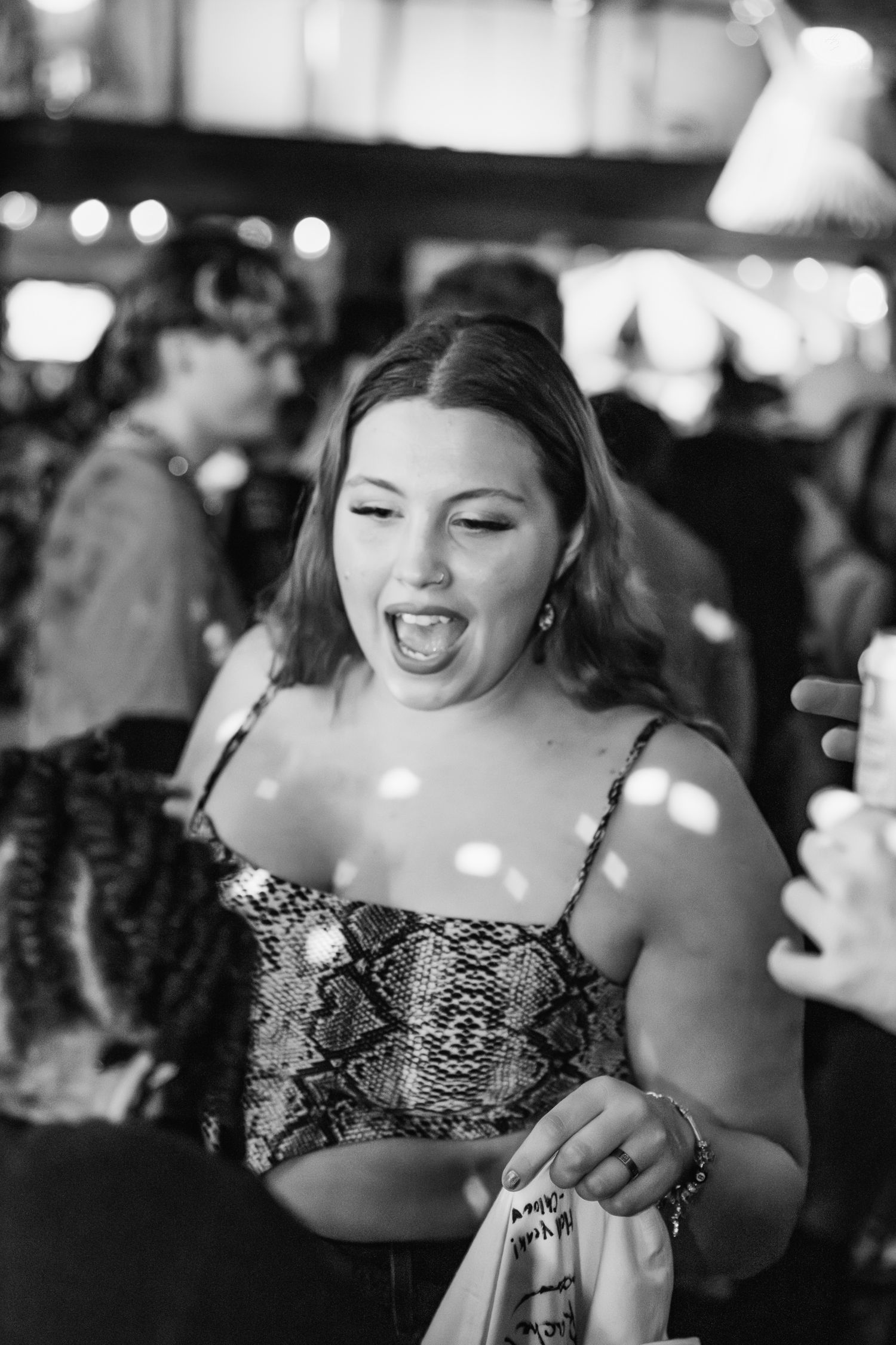Black and white photo of woman in snakeskin top laughing at a nightclub event.