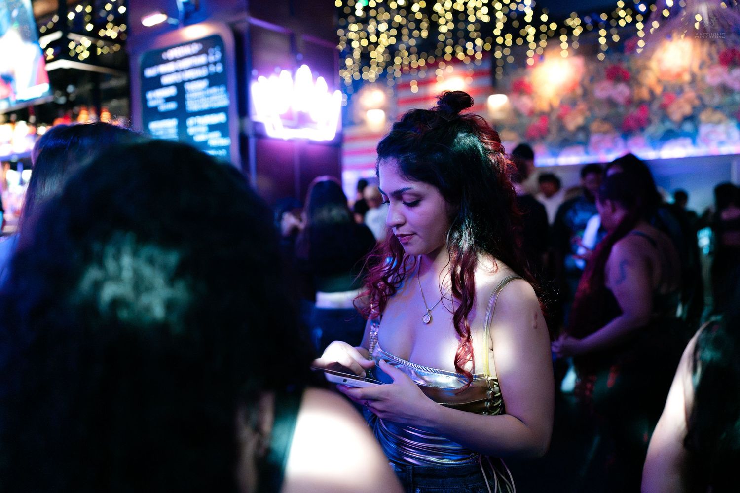 Woman in silver dress checking phone at vibrant nightclub event.