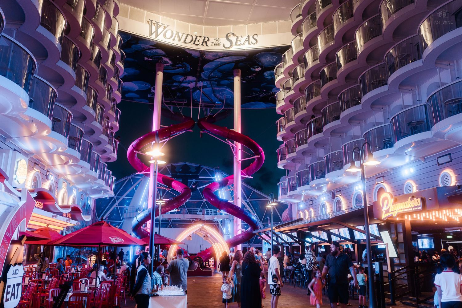 Stunning nighttime view of Wonder of the Seas cruise ship atrium with red waterslides and neon lights.