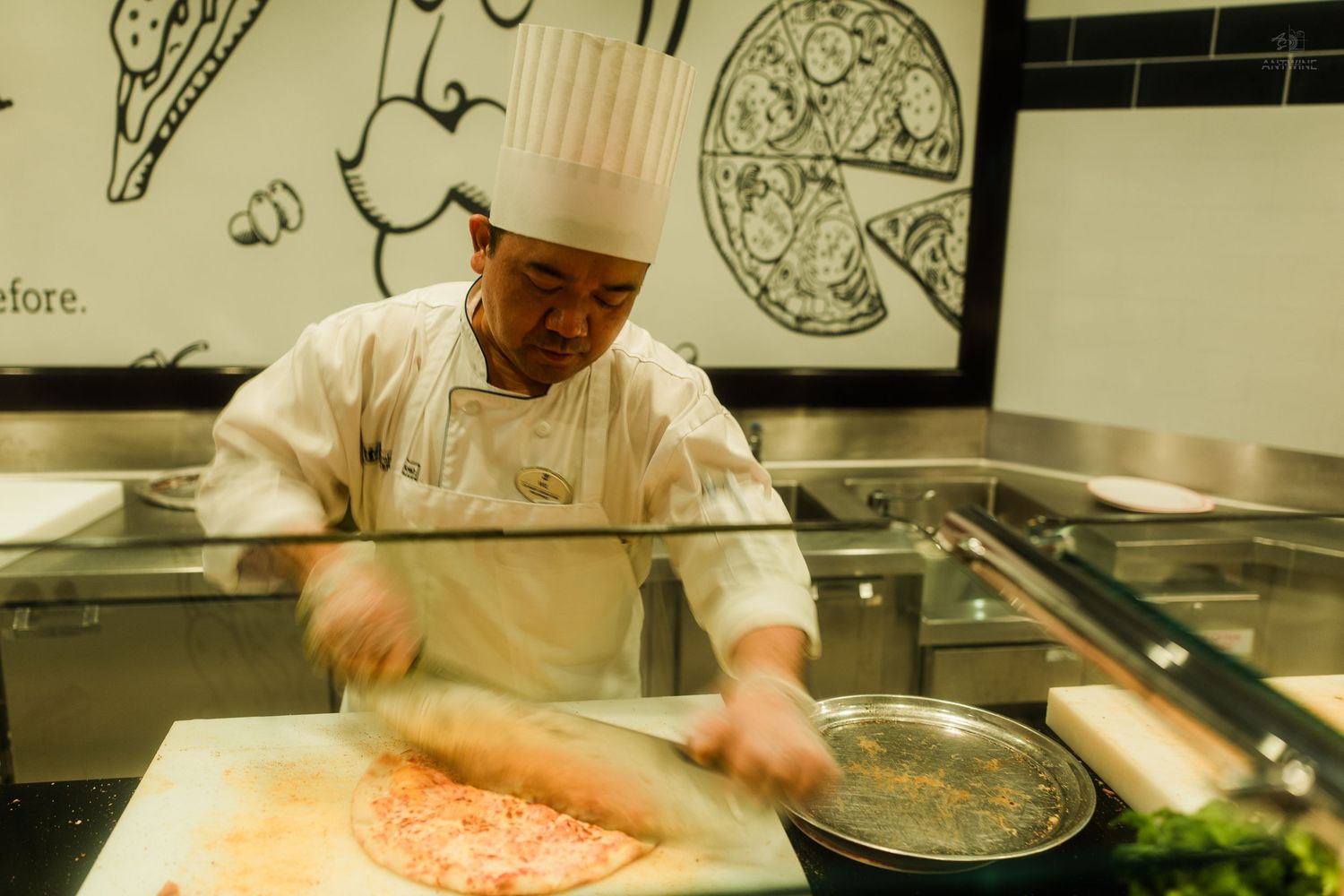 Professional chef in white uniform preparing pizza dough at a restaurant kitchen counter.
