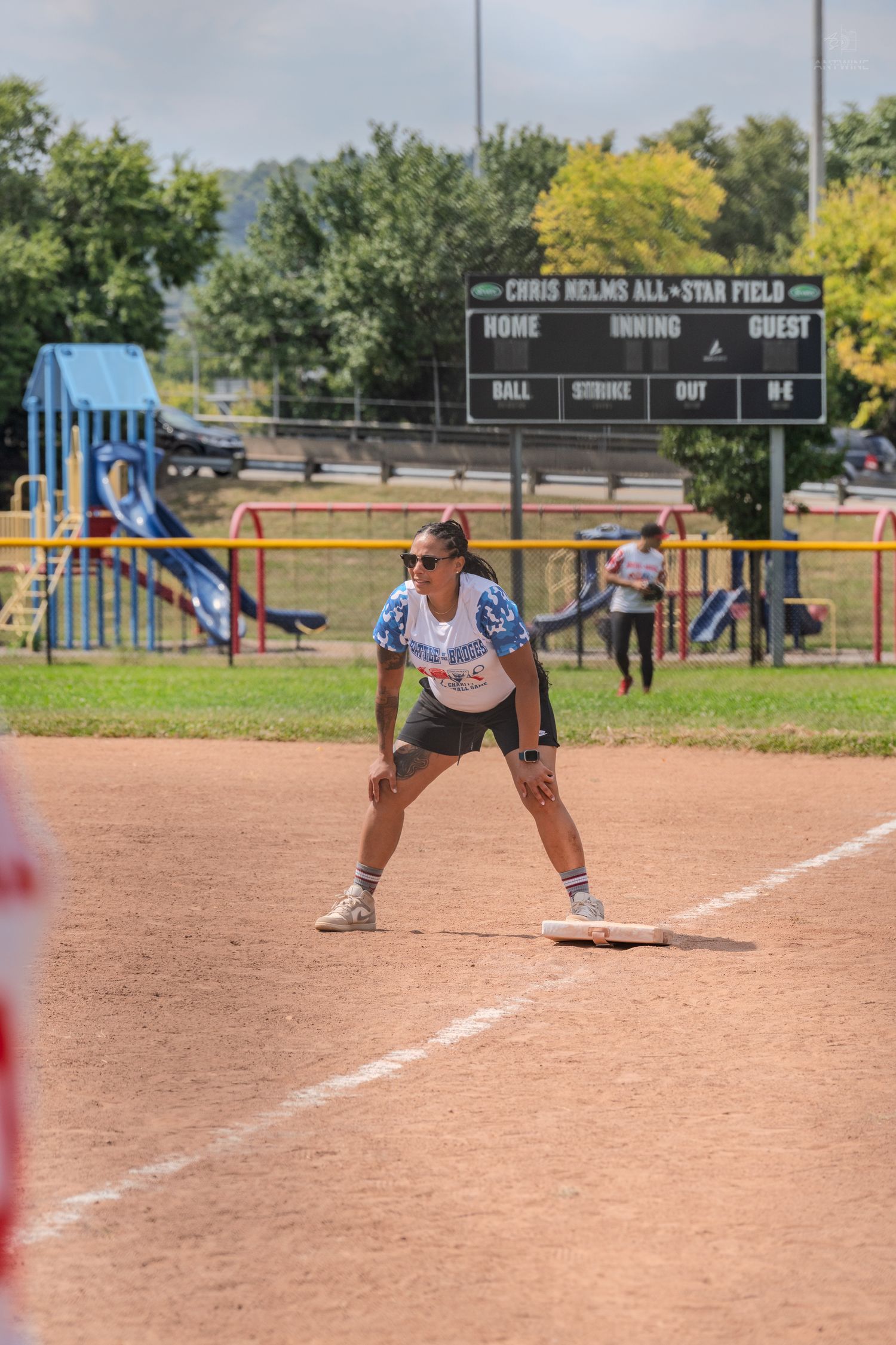 Female softball player in ready stance on base at Chris Helms All-Star Field during a charity game.