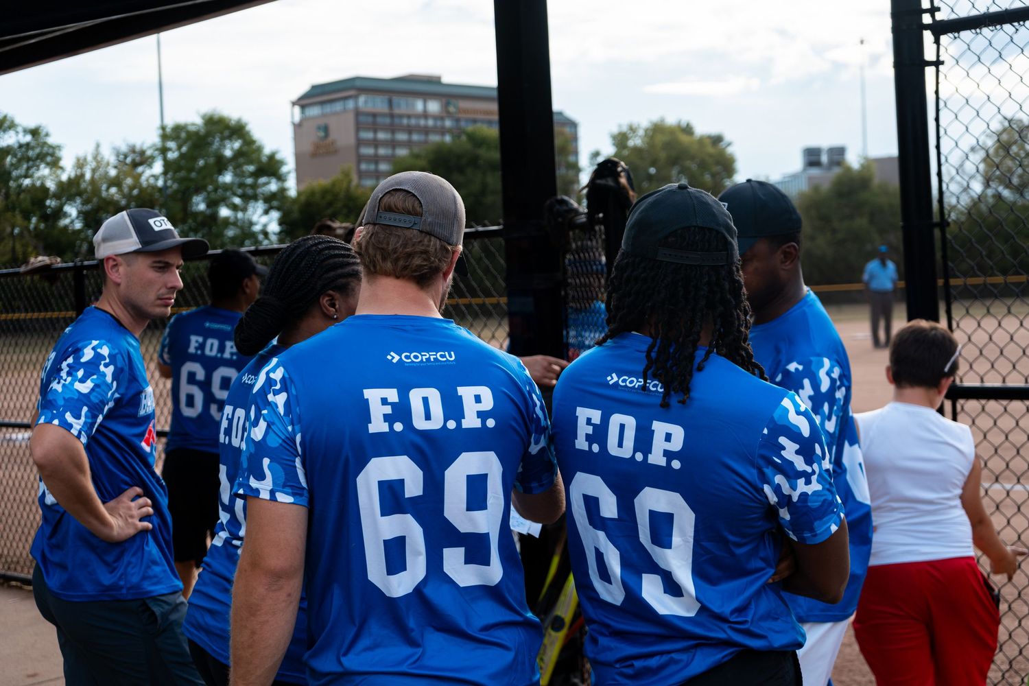 A group of players in blue F.O.P. number 69 jerseys huddle together at a softball game.