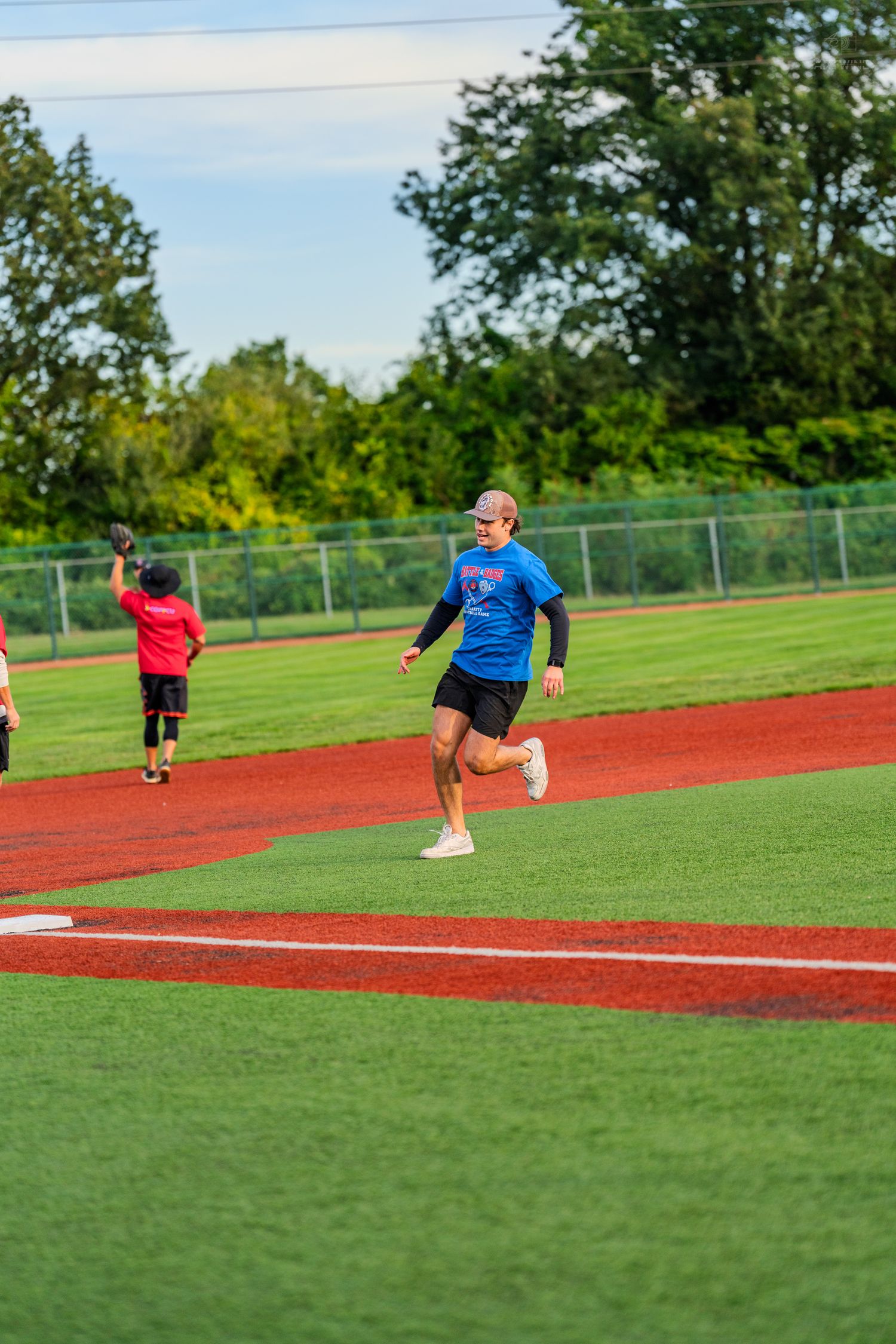 A player in a blue shirt runs the bases on a green turf baseball field during an outdoor game.