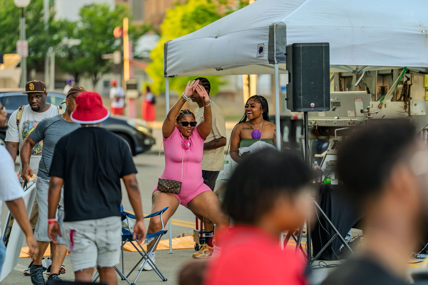 People dancing and celebrating at an outdoor community street festival with a stage and tent on a sunny day.