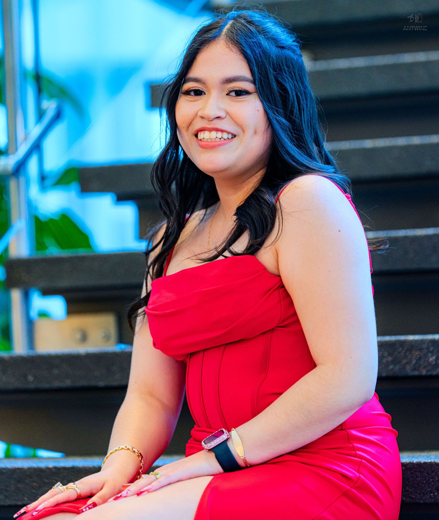 Smiling young woman in red strapless dress seated on stairs at formal event.