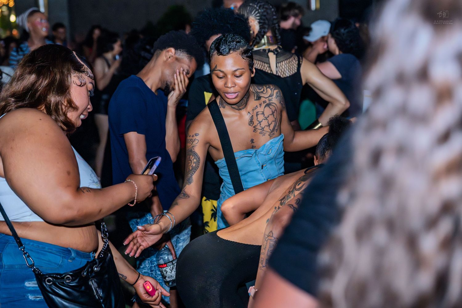 Tattooed woman dancing at an outdoor nightclub party event surrounded by crowd of people.