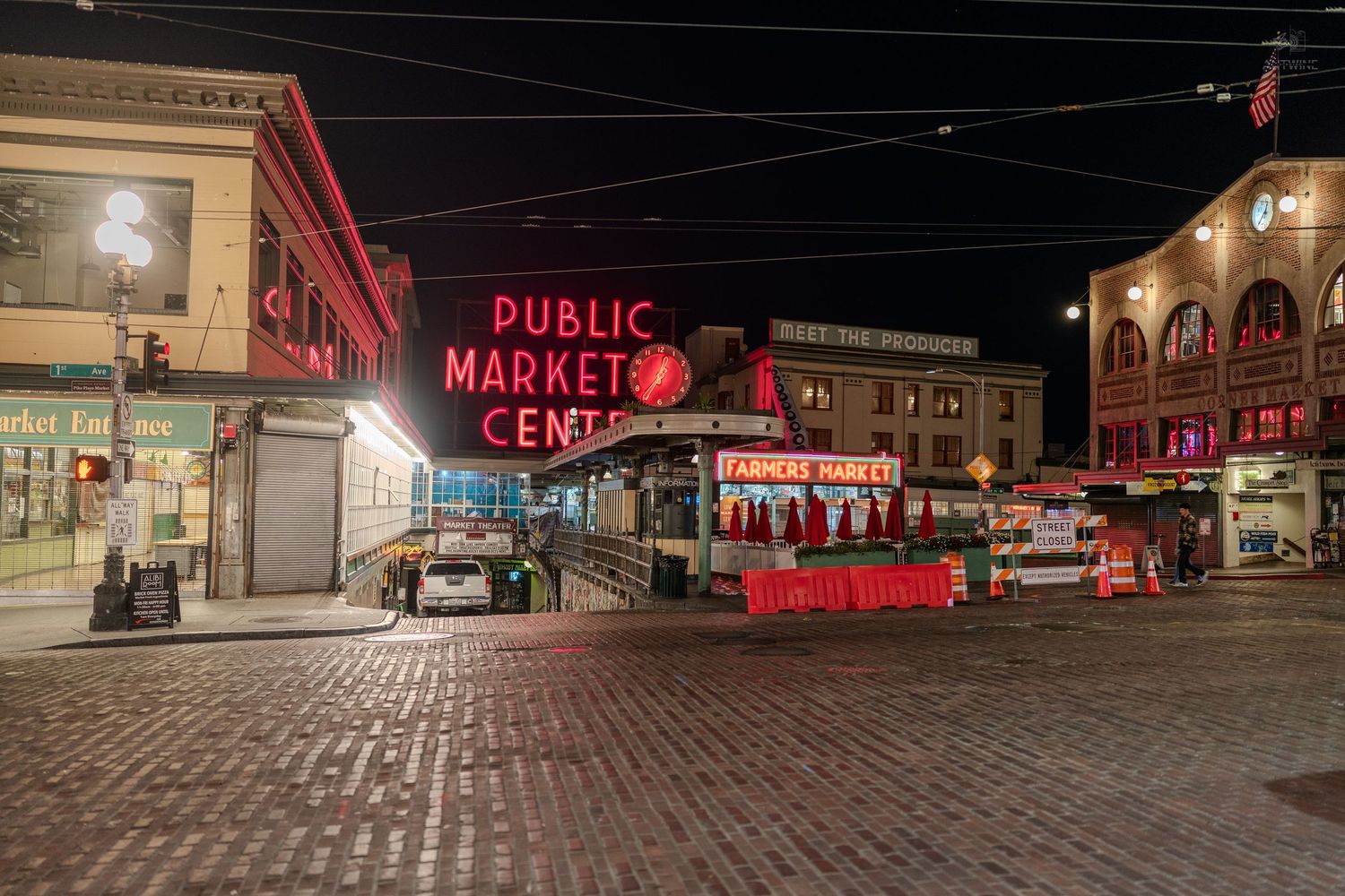 Pike Place Public Market Center illuminated at night with glowing red neon signs on cobblestone streets in Seattle.