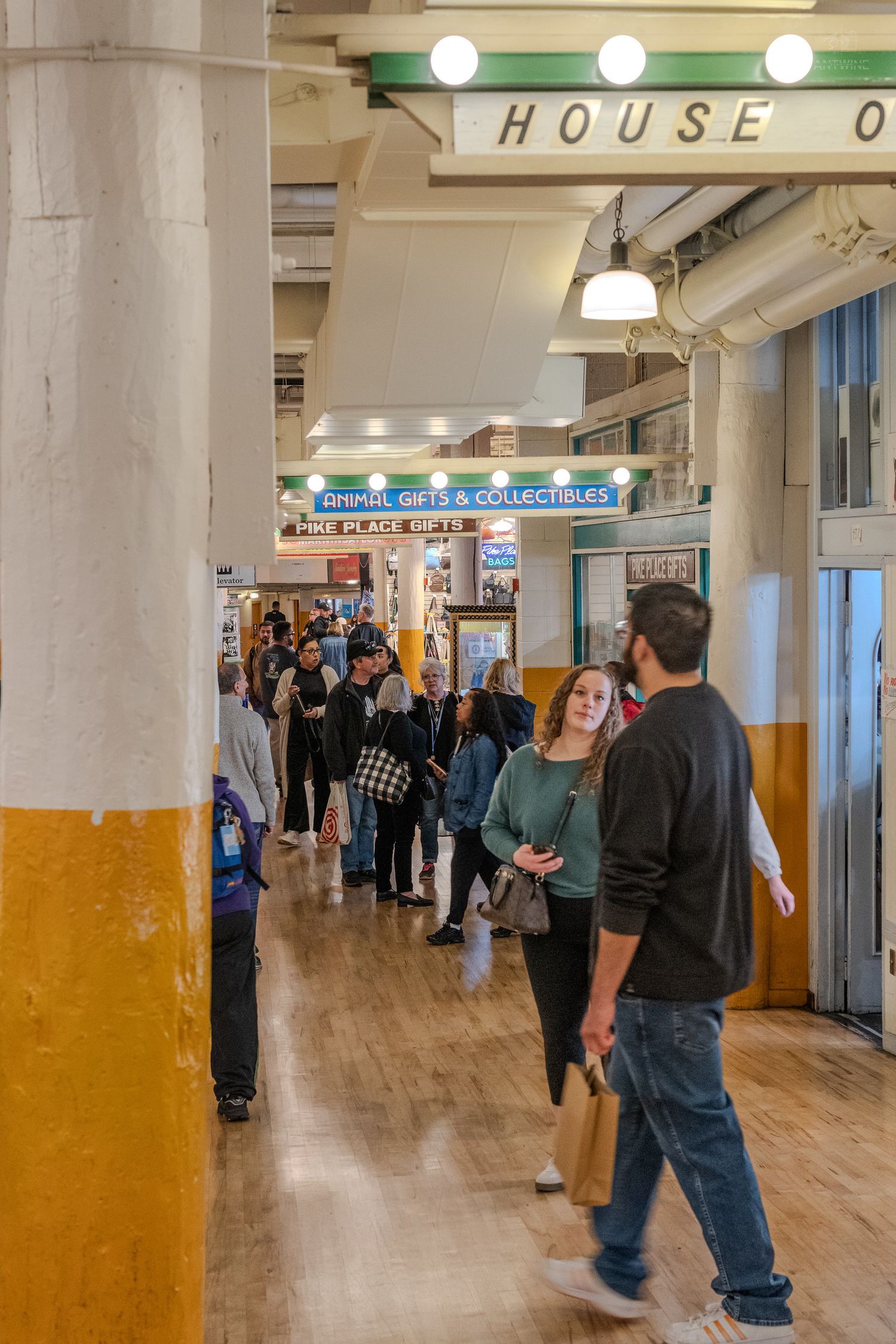 Busy indoor corridor at Pike Place Market with shoppers browsing gift stores and collectibles shops in Seattle.