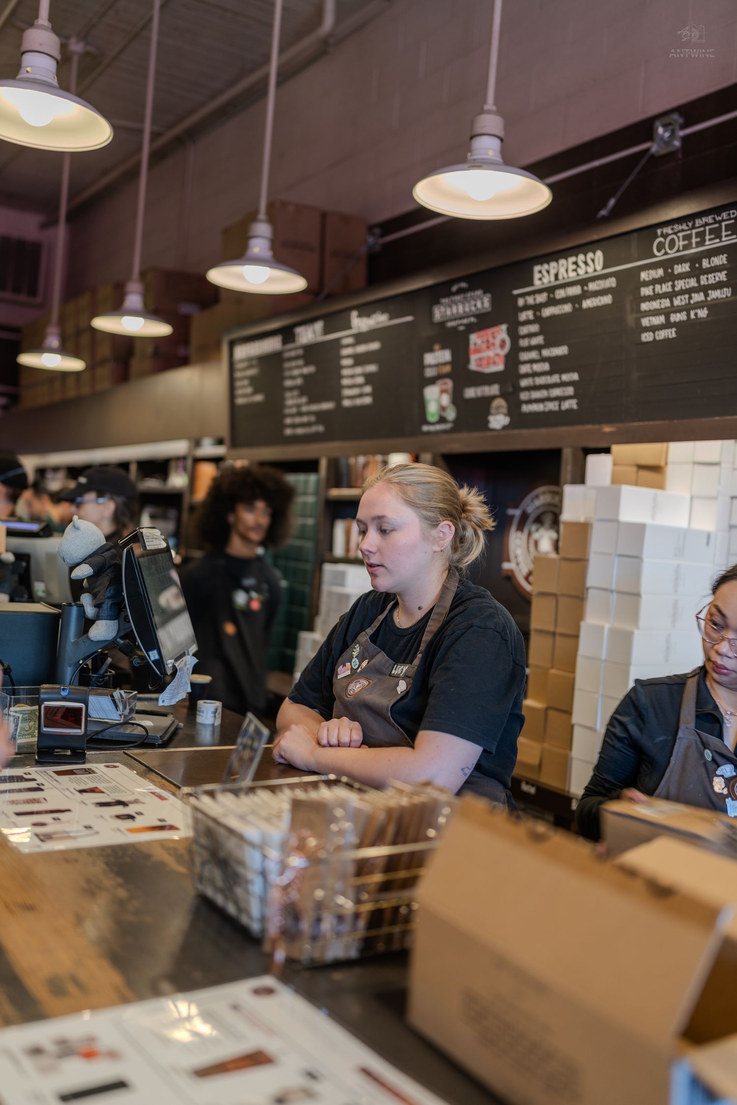 Baristas working behind the counter at a busy coffee shop with espresso menu boards overhead.