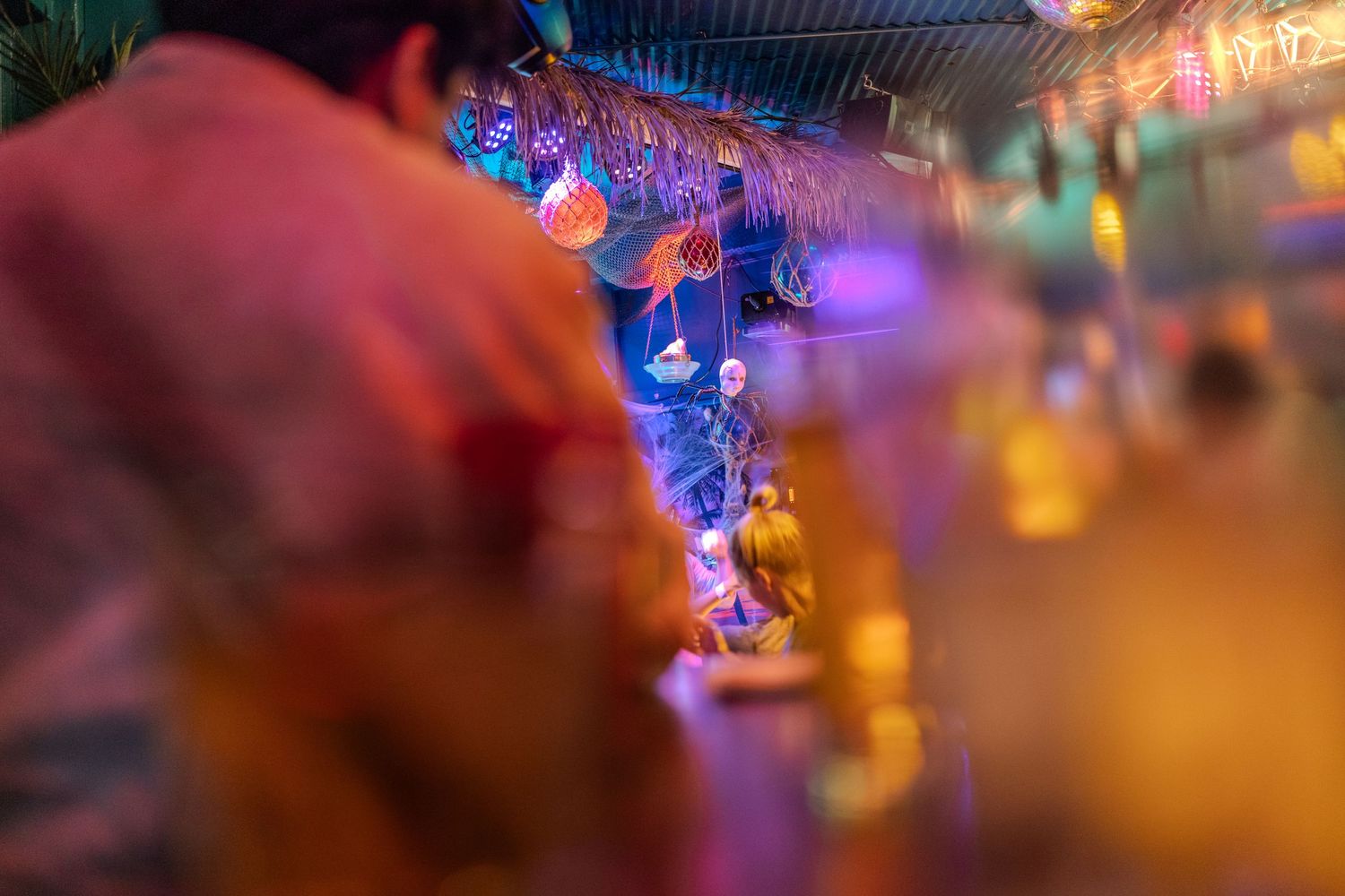 Colorful blurred bar scene with warm pink and orange lighting and hanging decorations.