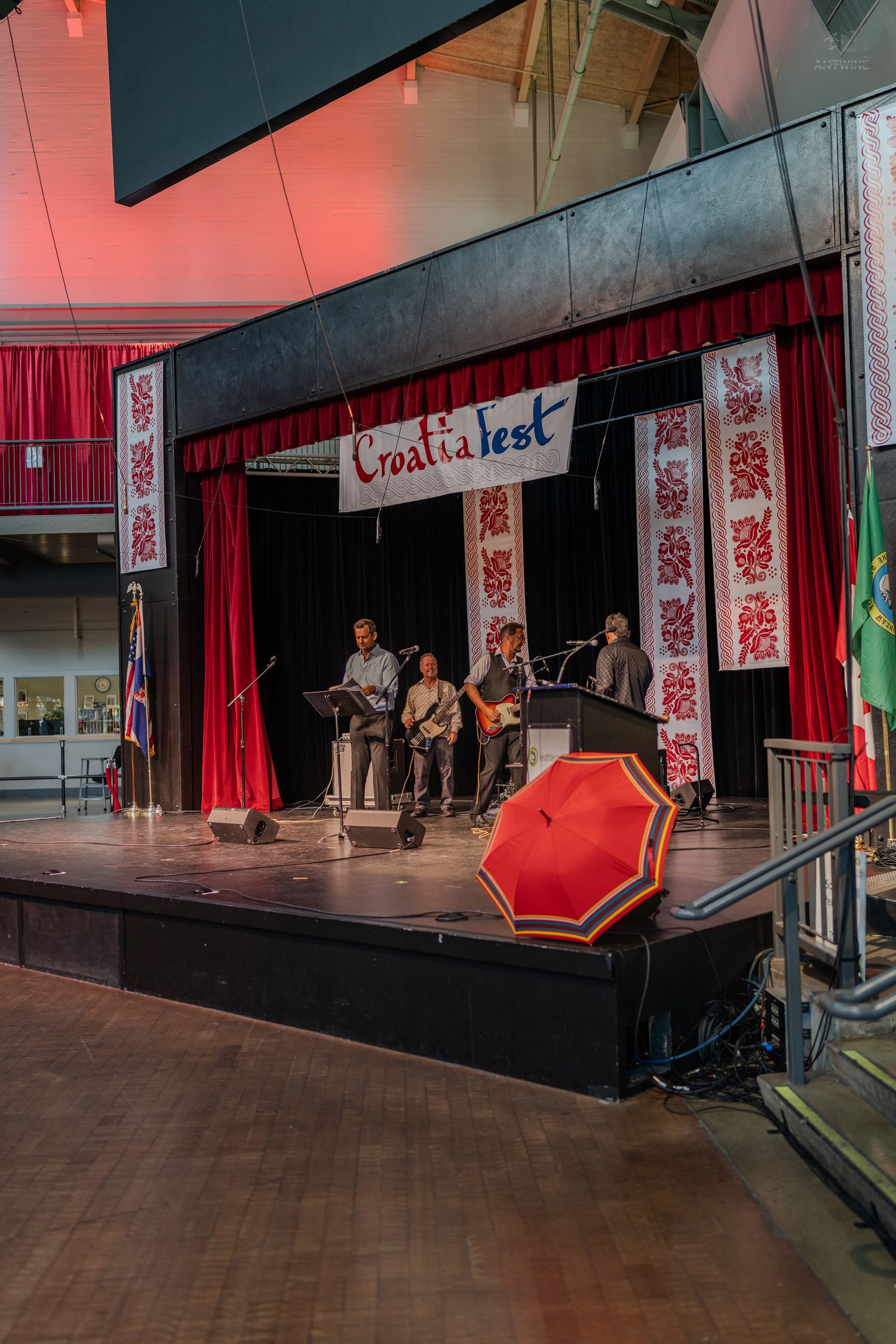Musicians perform at CroatiaFest on a decorated stage with red curtains, Croatian folk art banners, and a red umbrella.