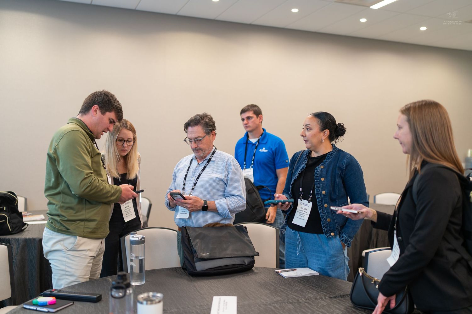A group of six professionals gather around a table examining documents at a business conference.