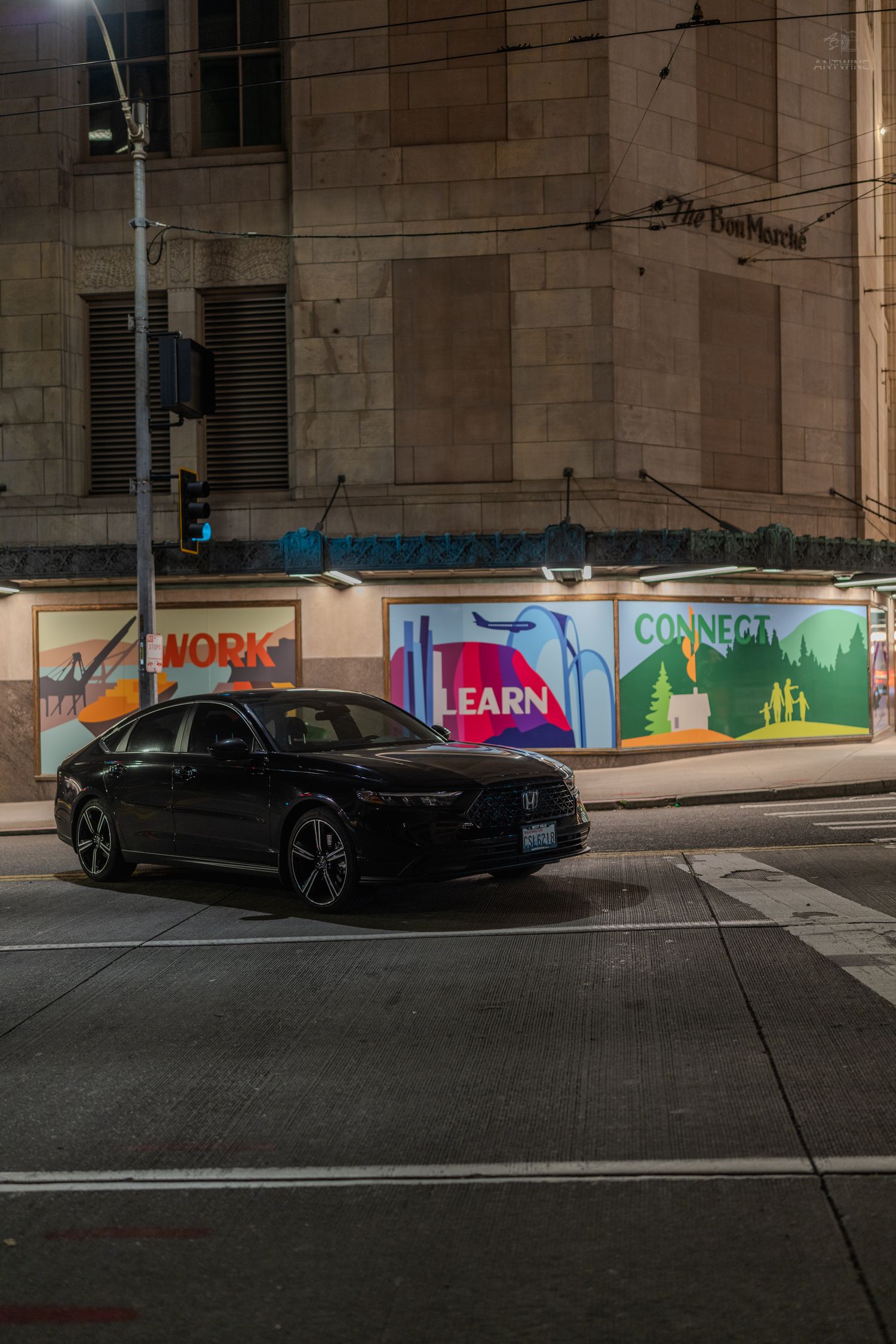 Black sedan parked at night near colorful murals reading Work, Learn, and Connect on urban building walls.