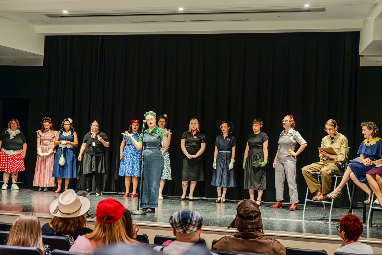 Group of performers in vintage costumes standing on stage during a theatrical production in a modern venue.
