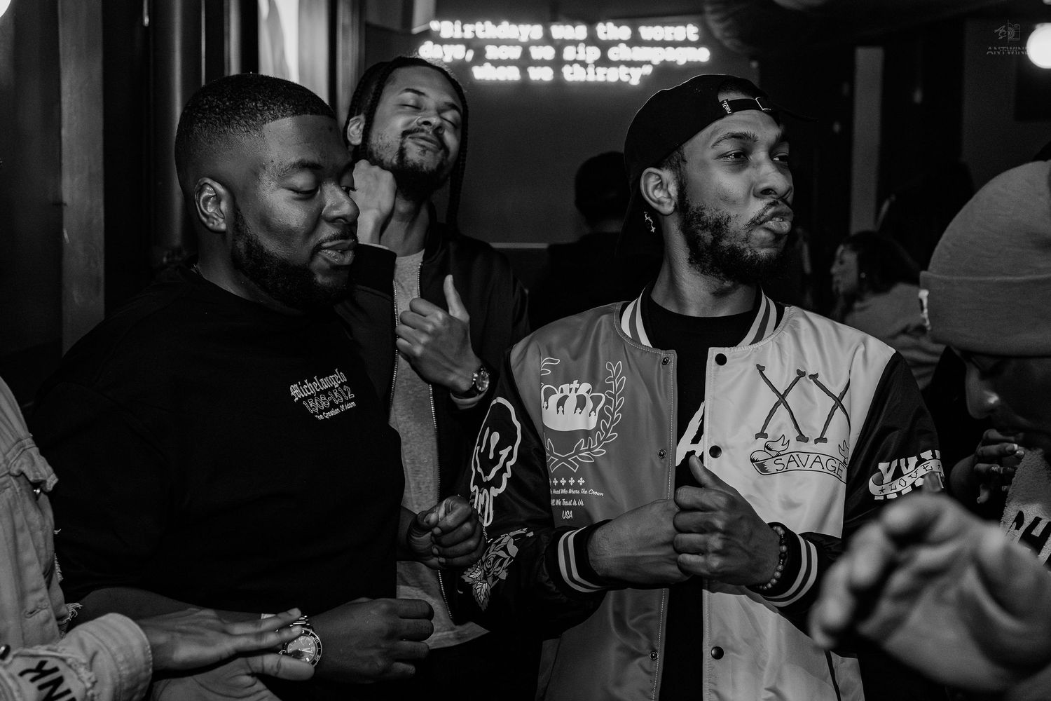 Black and white photo of three men socializing at a nightclub event, wearing casual streetwear.
