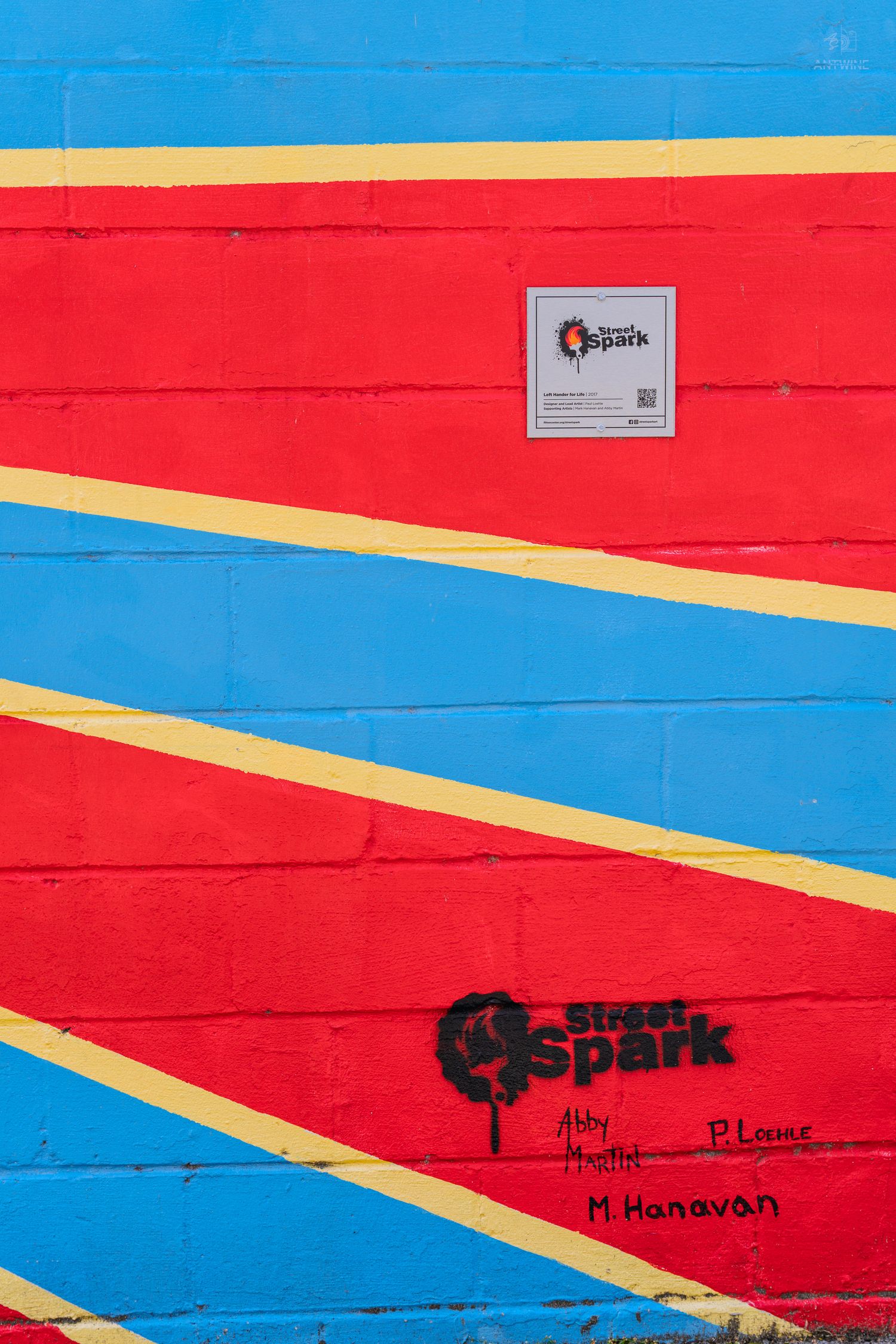 Colorful brick wall mural with red, blue, and yellow stripes featuring Street Spark graffiti art and signatures.