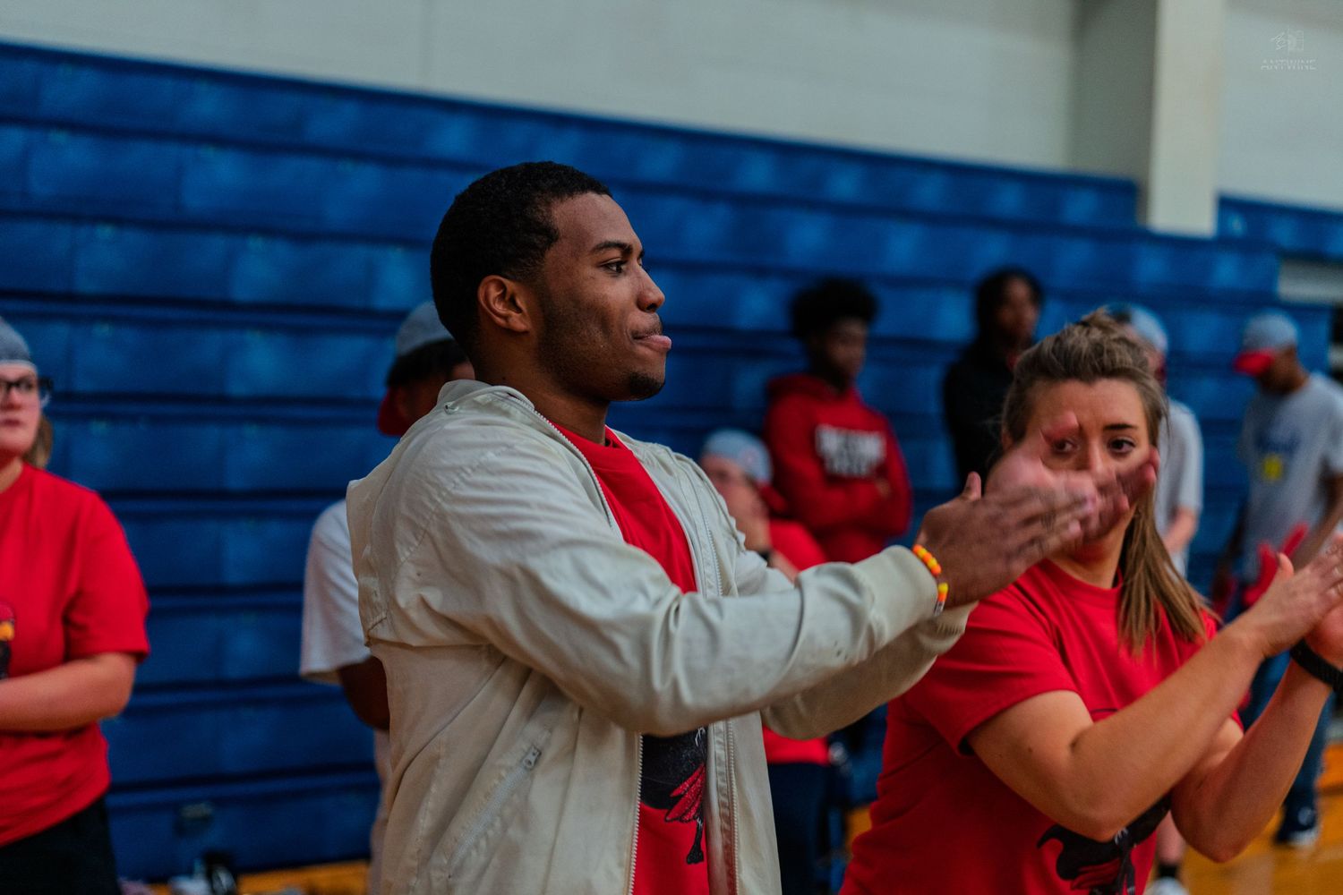 Two fans in red shirts clapping enthusiastically at an indoor basketball game in a blue gymnasium.