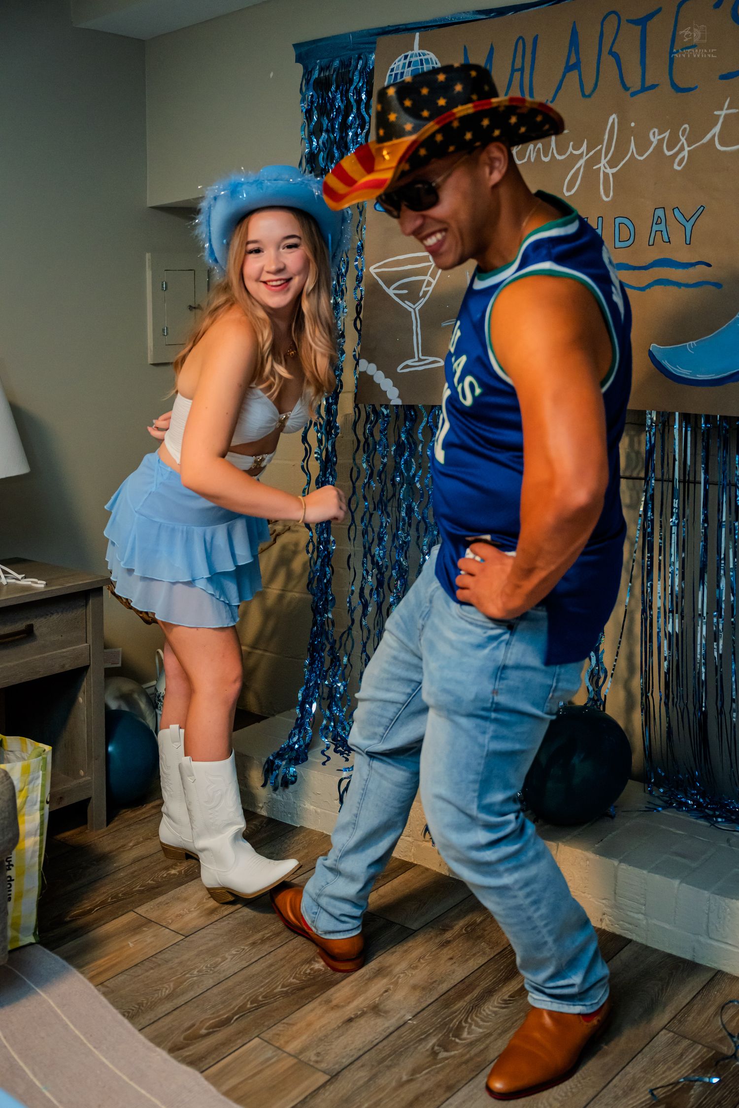 Laughing couple dancing together at a blue cowboy-themed 21st birthday celebration with party decorations.