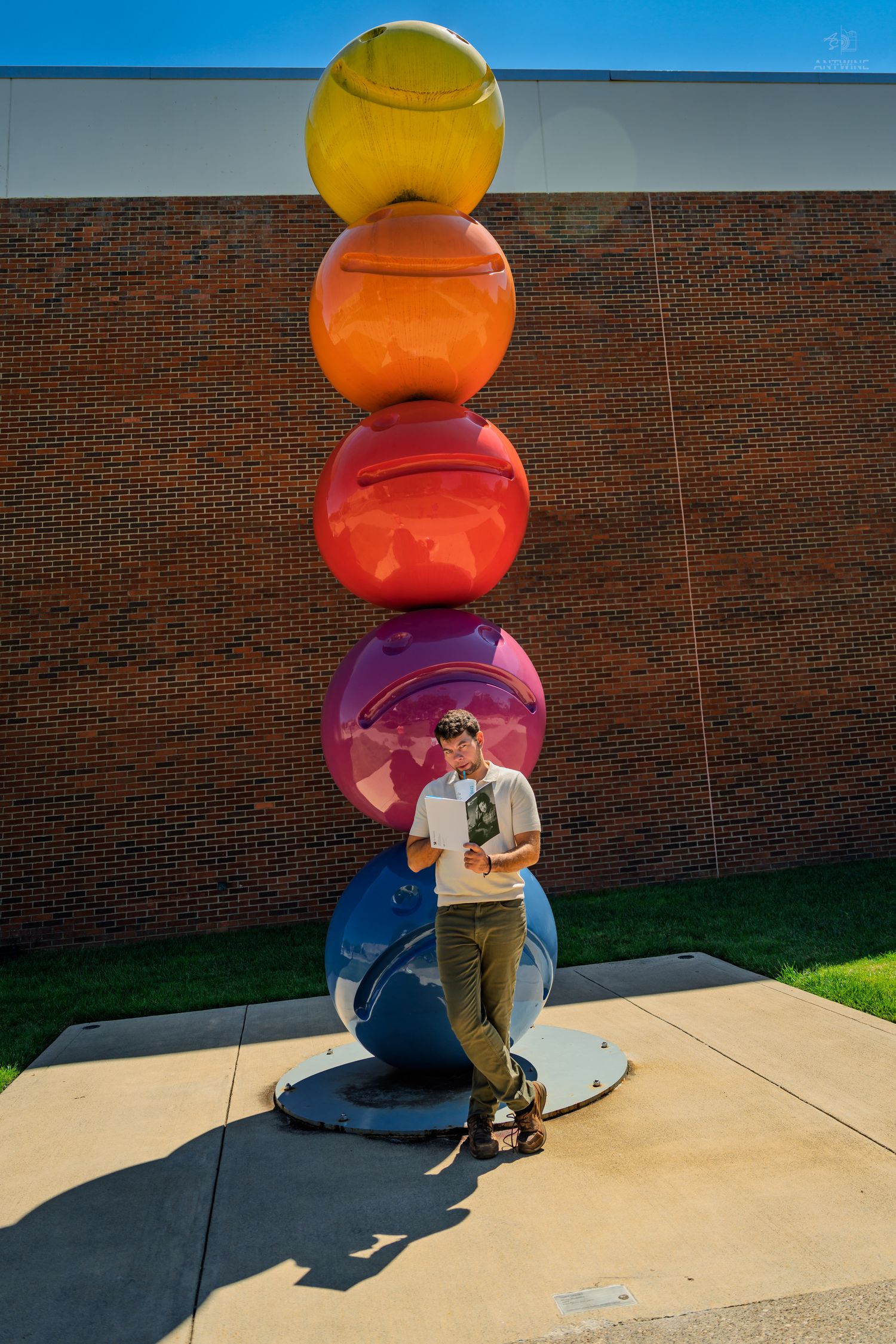 A man in a white shirt leans against a large blue sphere at the base of a colorful stacked ball sculpture.