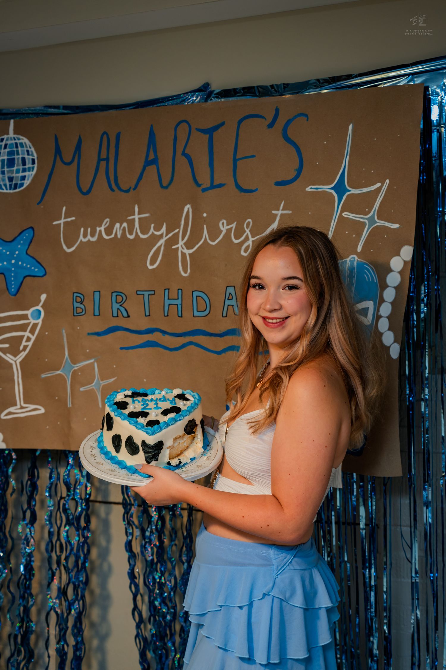 Smiling birthday girl holds decorated heart cake at Malarie's 21st birthday party with blue decor.
