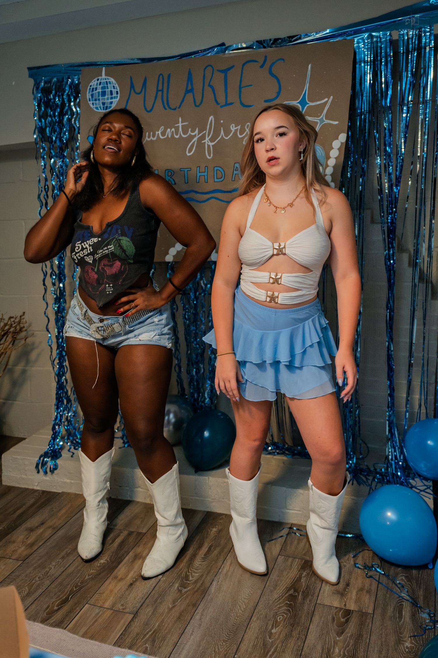 Two women in white cowboy boots pose at Malarie's 21st birthday party with blue balloon decorations.