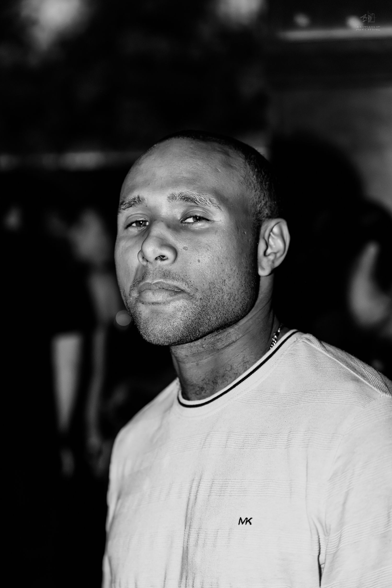 Black and white portrait of a man in a Michael Kors shirt at a nightclub looking upward.