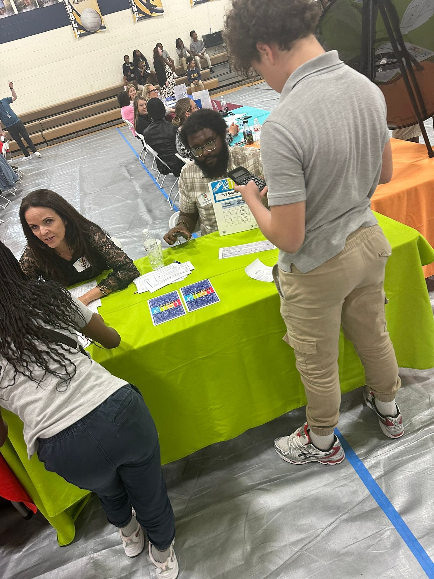 Students and adults interact at a school career fair booth with a bright green table in a gymnasium.